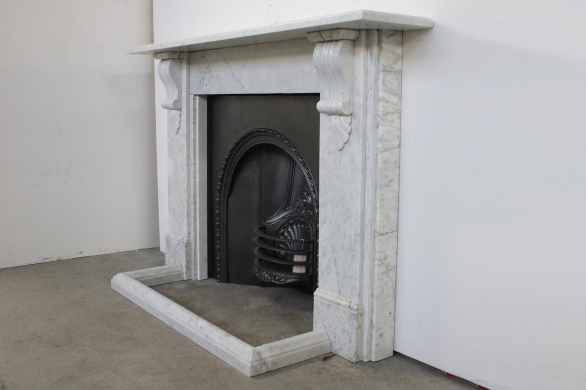 A substantial antique Victorian fireplace surrounds in Carrara marble with carved corbeled supporting the shelf, English, circa 1860.
See images for detailed sizes.
Pictured with an original cast iron insert and marble fender, both priced