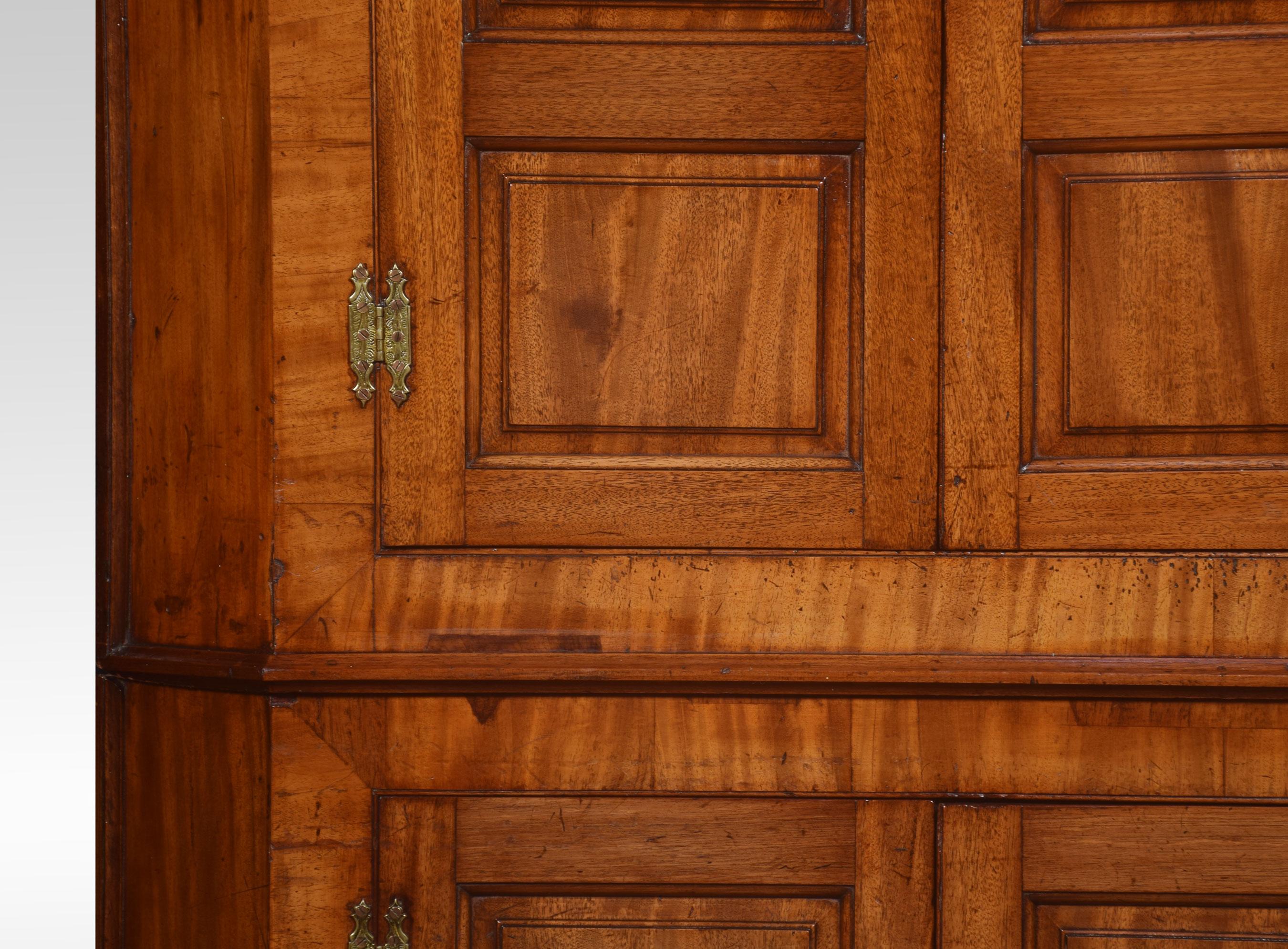 Ein beachtlicher, bodenstehender Eckschrank aus Mahagoni im Landhausstil. Das profilierte Gesims über einem Paar gewölbter, feldförmiger Türen, die einen Innenraum mit Regalen und drei kleinen Schubladen umschließen. Das Unterteil ist mit einem Paar