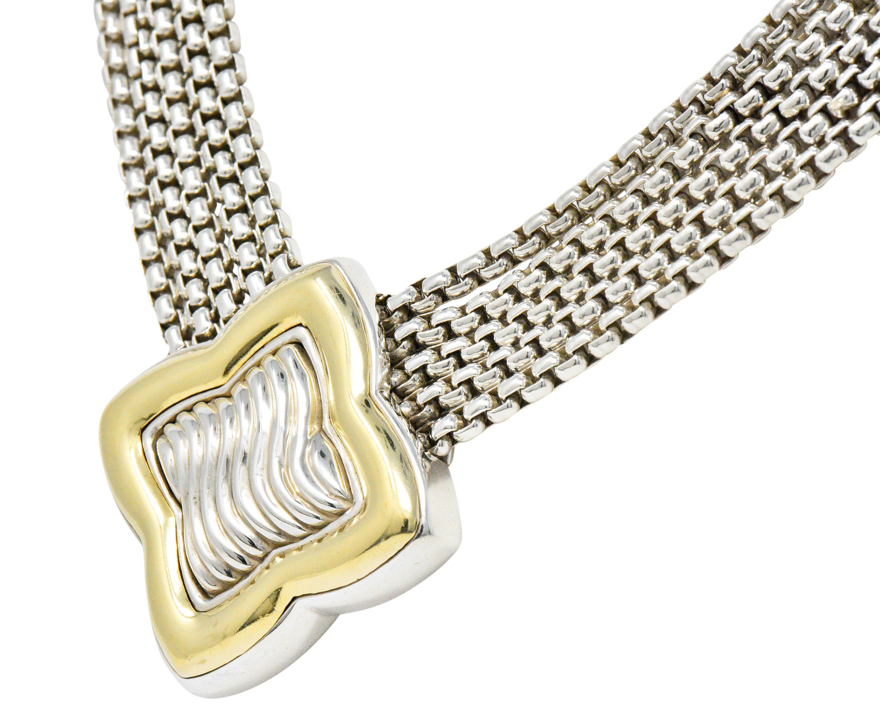 Mehrreihige Halskette mit einer großen, vierblättrigen Station in der Mitte mit tief geriffeltem Silber 
umgeben von einer hochglanzpolierten Goldlünette

Aufgehängt an fünf Strängen einer silbernen Kastenkette

Vervollständigt durch Endkappen mit