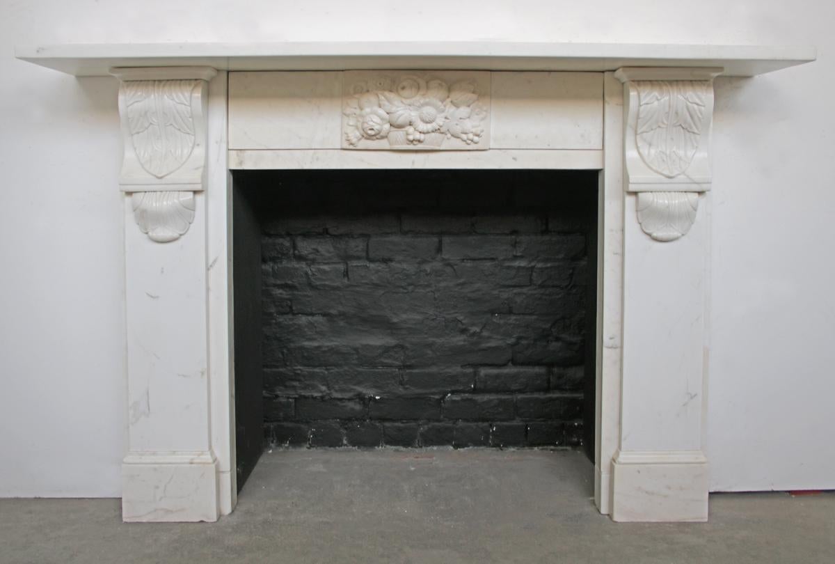 A substantial early Victorian fire surround in statuary marble. Well carved acanthus corbels sit above plain jambs and flank a stepped frieze centered with a deeply carved tablet depicting a basket of flowers and fruit. Circa 1840.

For detailed