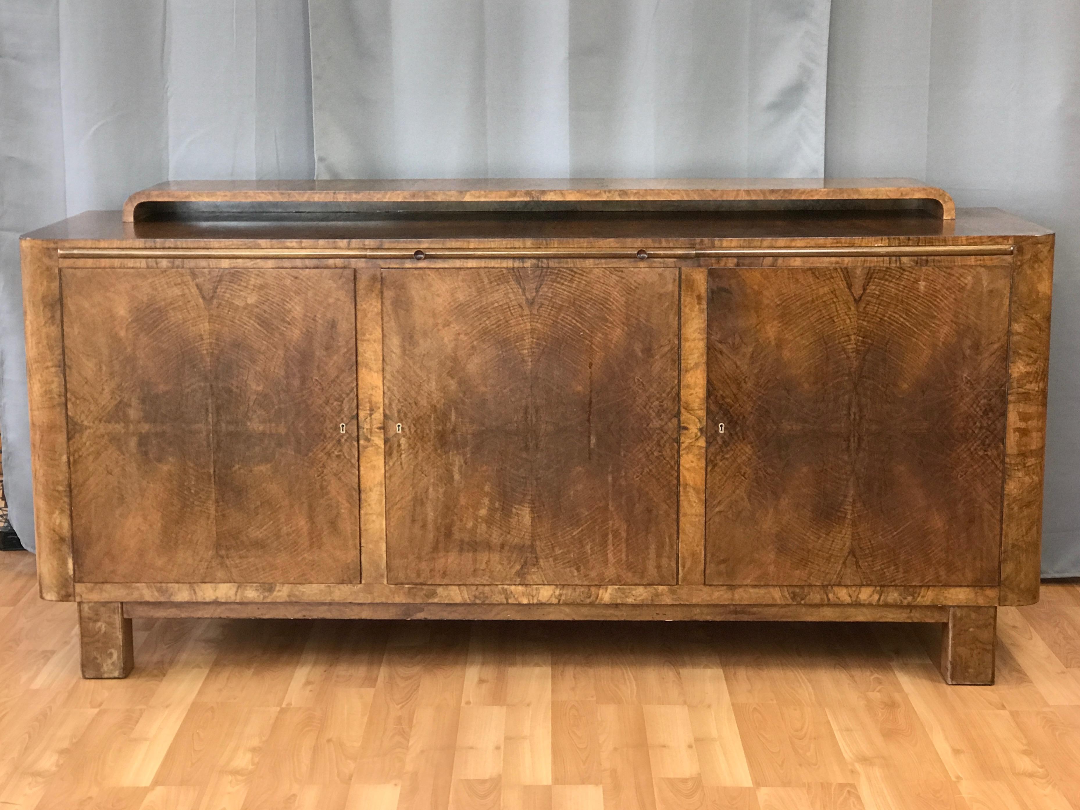An exceptional and expansive German Art Deco or Art Moderne walnut buffet or sideboard, circa late 1930s-early 1940s.

Streamlined form distinguished by strikingly figured bookmatched curly French walnut veneer. Three spacious locking cabinets (key