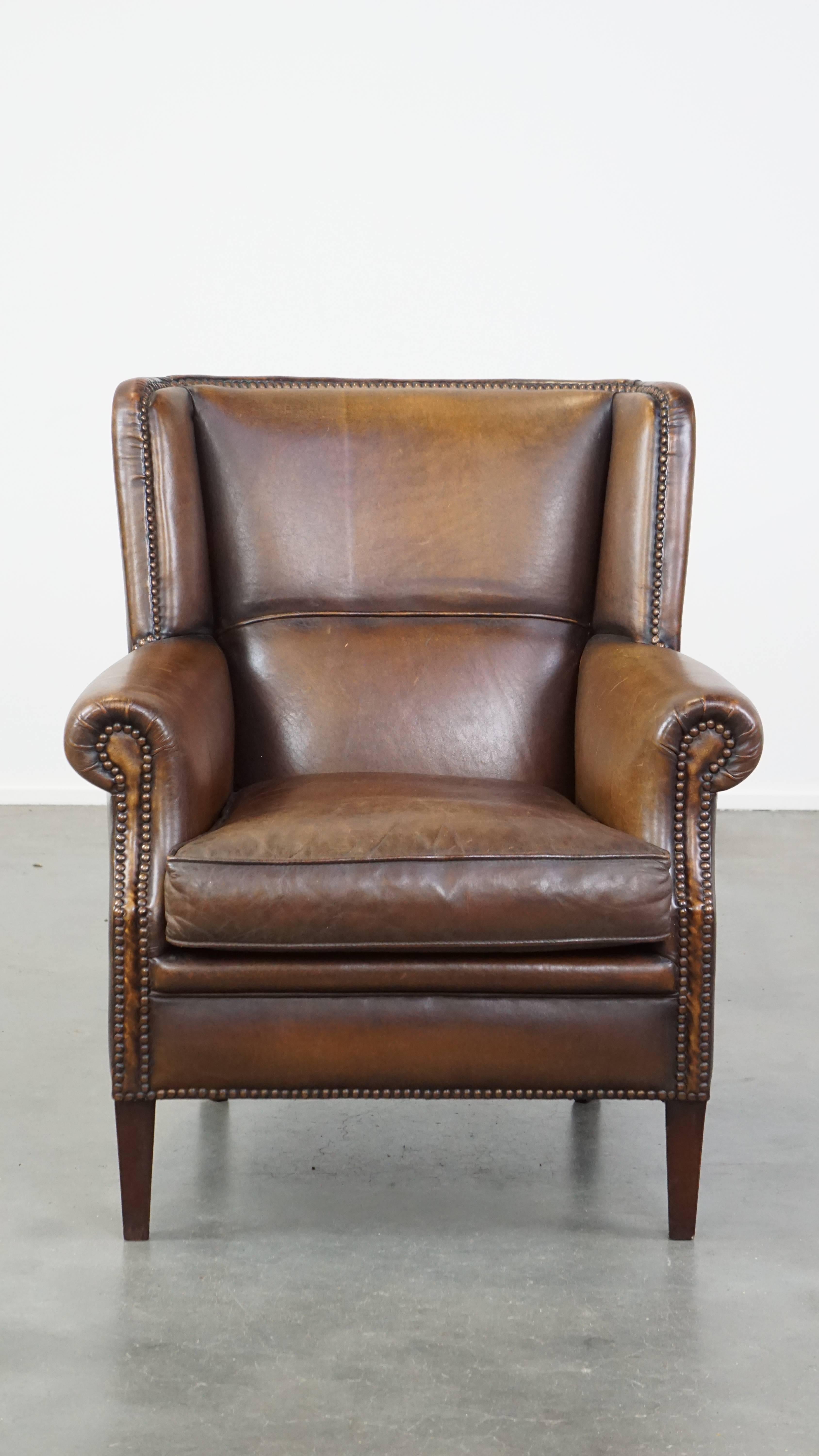 Questa sottile poltrona in pelle di pecora si adatta facilmente a quasi tutti gli interni. Grazie al colore scuro, alla parte superiore diritta dello schienale e alla finitura con chiodi decorativi, ha un aspetto robusto ma raffinato. Questa