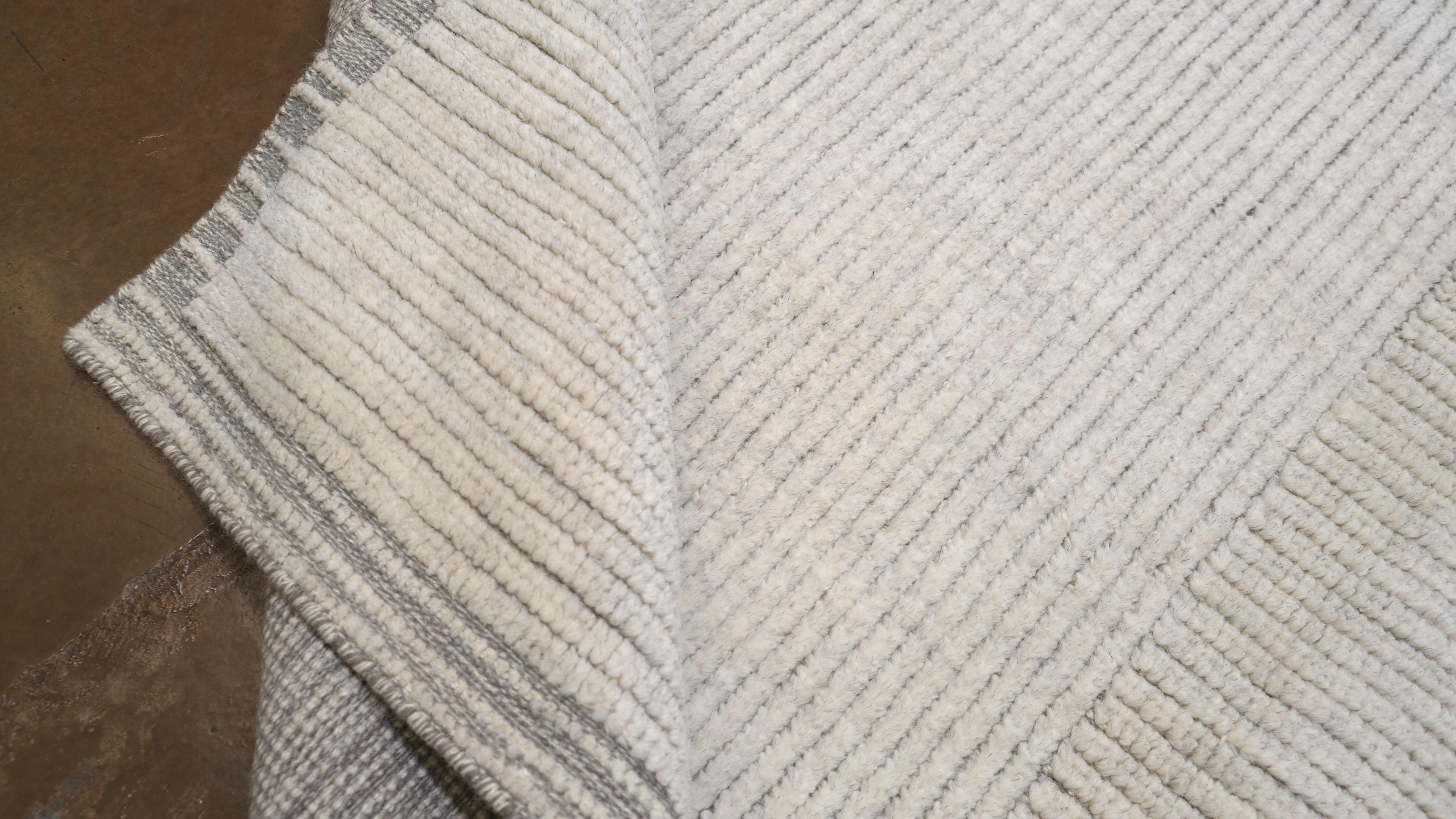 Il présente un subtil quadrillage rayé dans des tons doux d'ivoire et de gris. L'esthétique minimaliste de ce tapis respire la sophistication, ce qui en fait un choix idéal pour les espaces contemporains, transitionnels ou d'inspiration