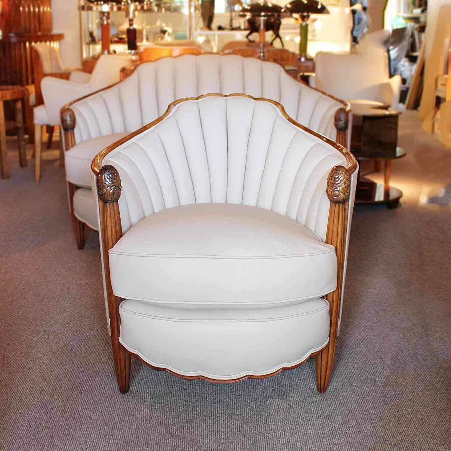 An Art Deco three piece suite comprising two seater settee and two armchairs. Solid walnut frames with tapering legs to front and carved detail. Iconic Süe et Mare scalloped edging throughout. Upholstered in cream leather and Alcantara