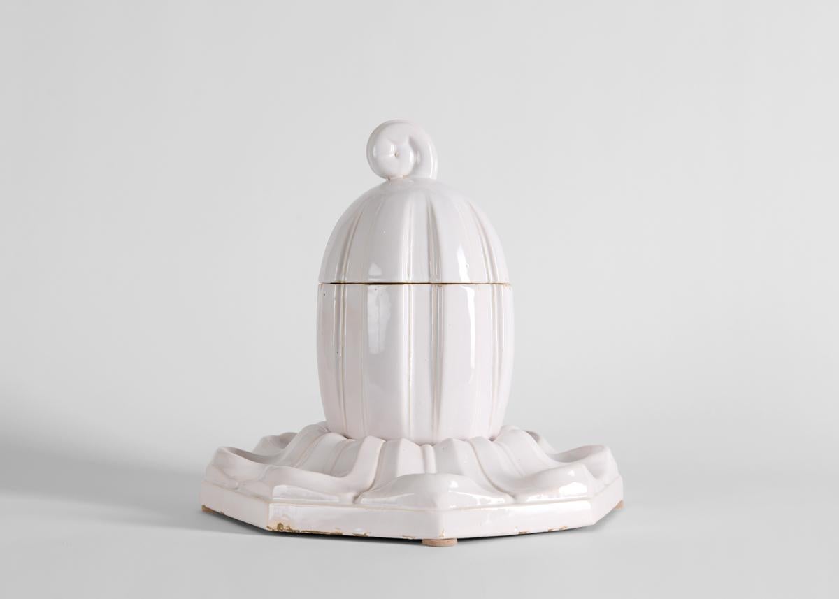 Designed to hold tobacco and pipes, this lidded bowl is set in an elegant base, executed in glazed faïence, exhibits Süe et Mare's dual focus on heritage and modernity. The pair were known for updating the Louis-Philippe era, which they considered