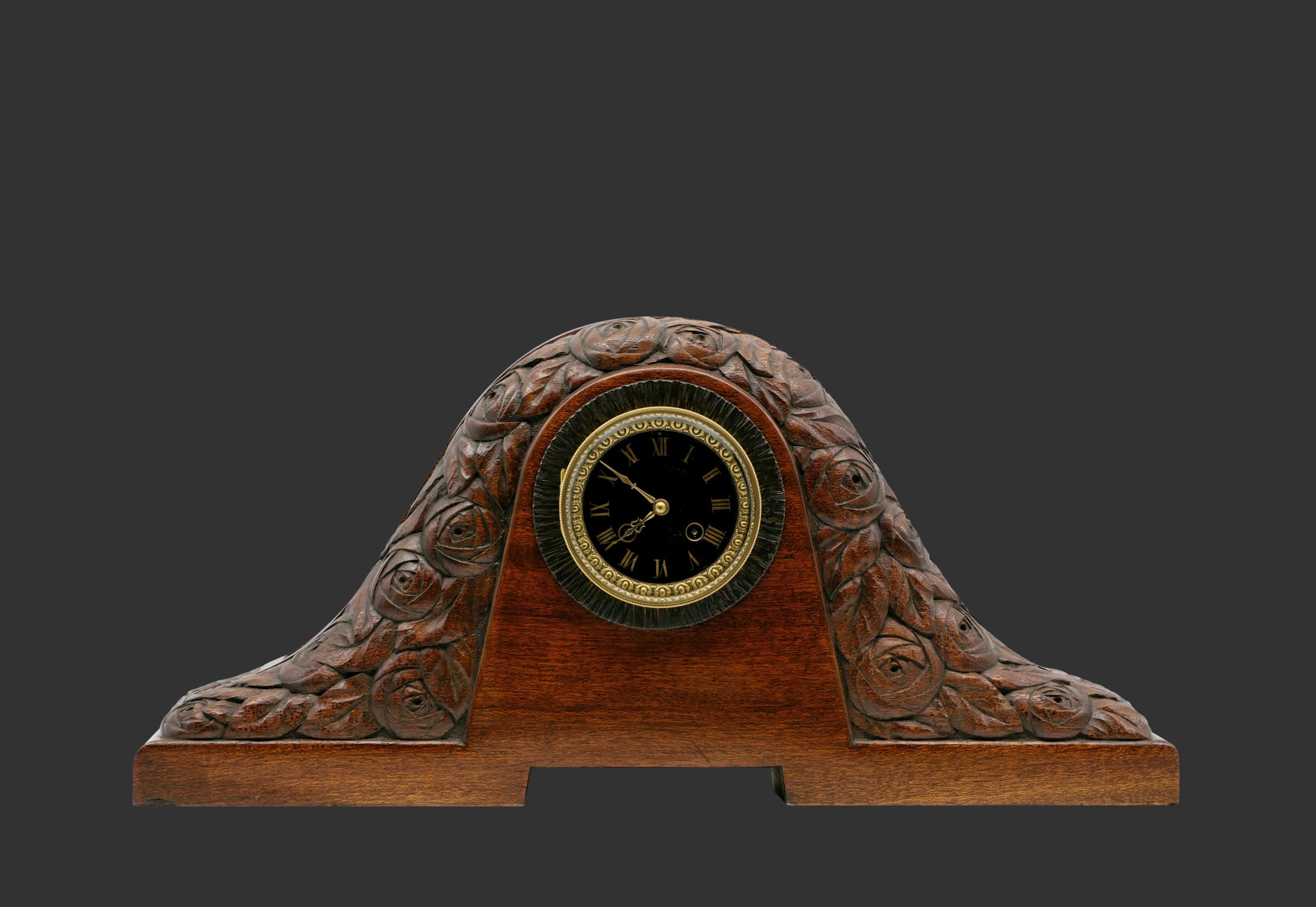 French Art Deco table / mantel clock in the taste of Süe & Mare, France, ca.1920. Carved rose garland ornamentation. Exotic wood (palm wood?), rare of this wood. 8 days movement. Two beveled glass doors. Height: 11