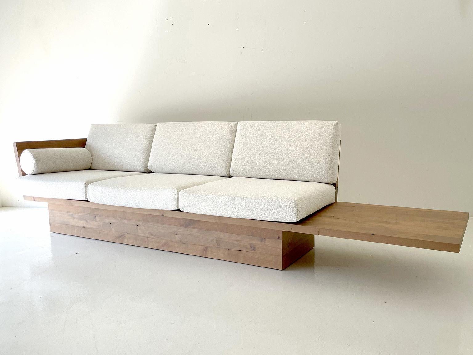 Ce canapé moderne en bois Suelo avec socle est magnifiquement construit en bois massif dans l'Ohio, aux États-Unis. La silhouette du canapé est simple, moderne et élégante, avec des coussins de siège et de dossier confortables. C'est le canapé