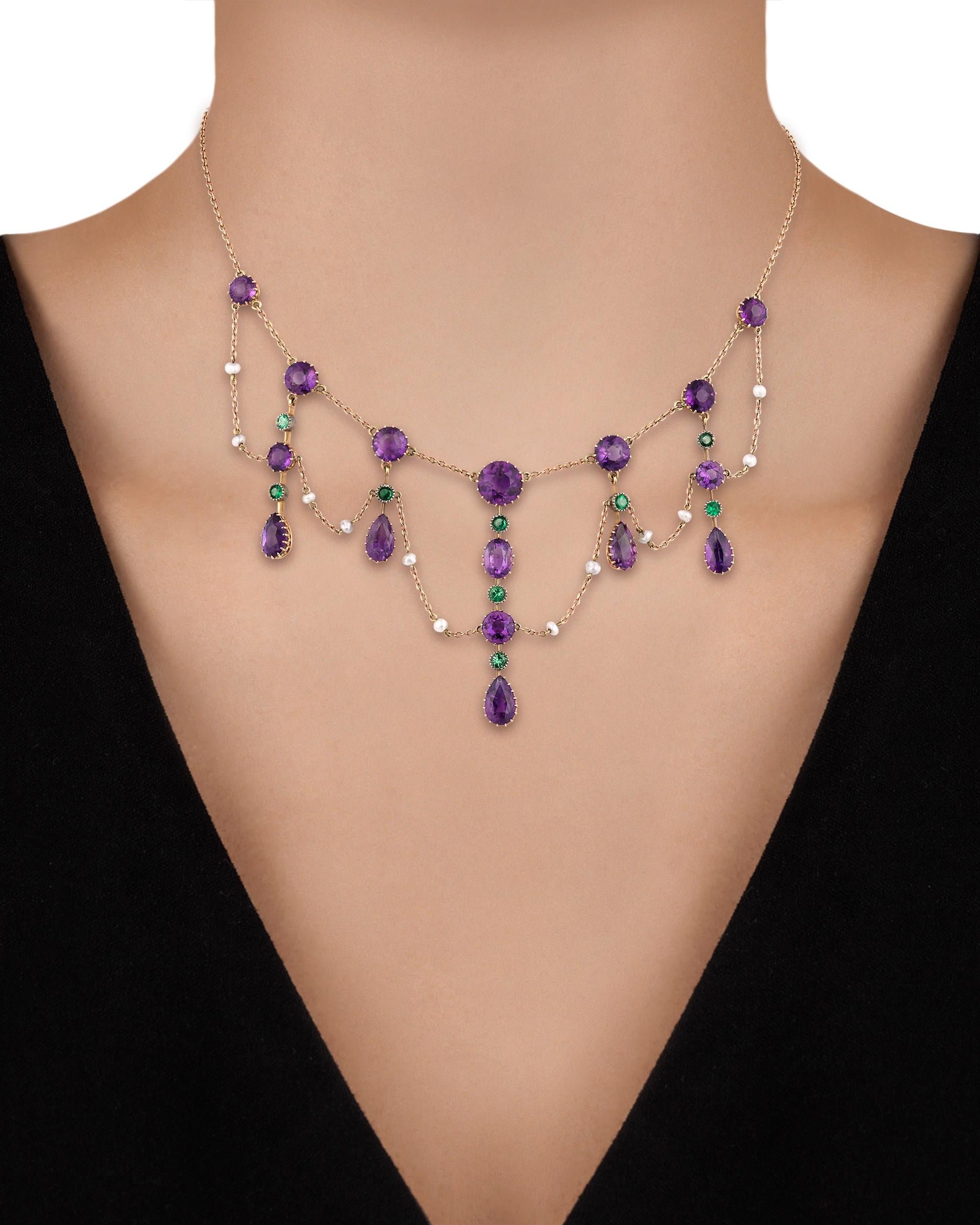 A total of 16 richly colored round and pear-shaped amethysts, nine round demantoid garnets and seed pearls combine to form a colorful garland in this British suffragette collar necklace. Suffragettes wore certain colors synonymous with the movement,