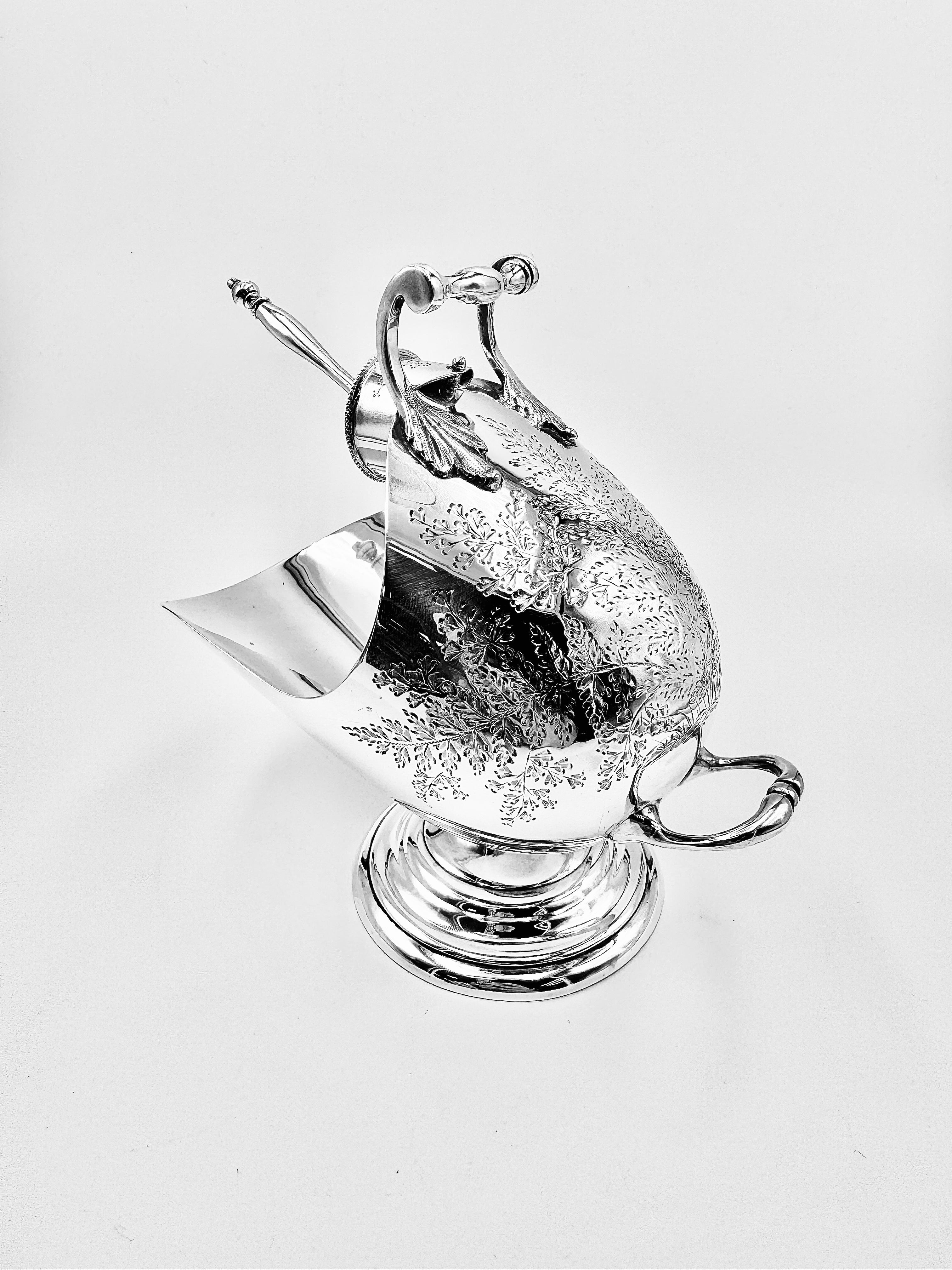 A Victorian silver sugar scuttle with matching spoon, made by Mappin & Webb, London, 1900. Designed in the form of a coal scuttle, the body is engraved with scrolling foliage and rests on a raised circular foot. With maker’s mark of Mappin & Webb on