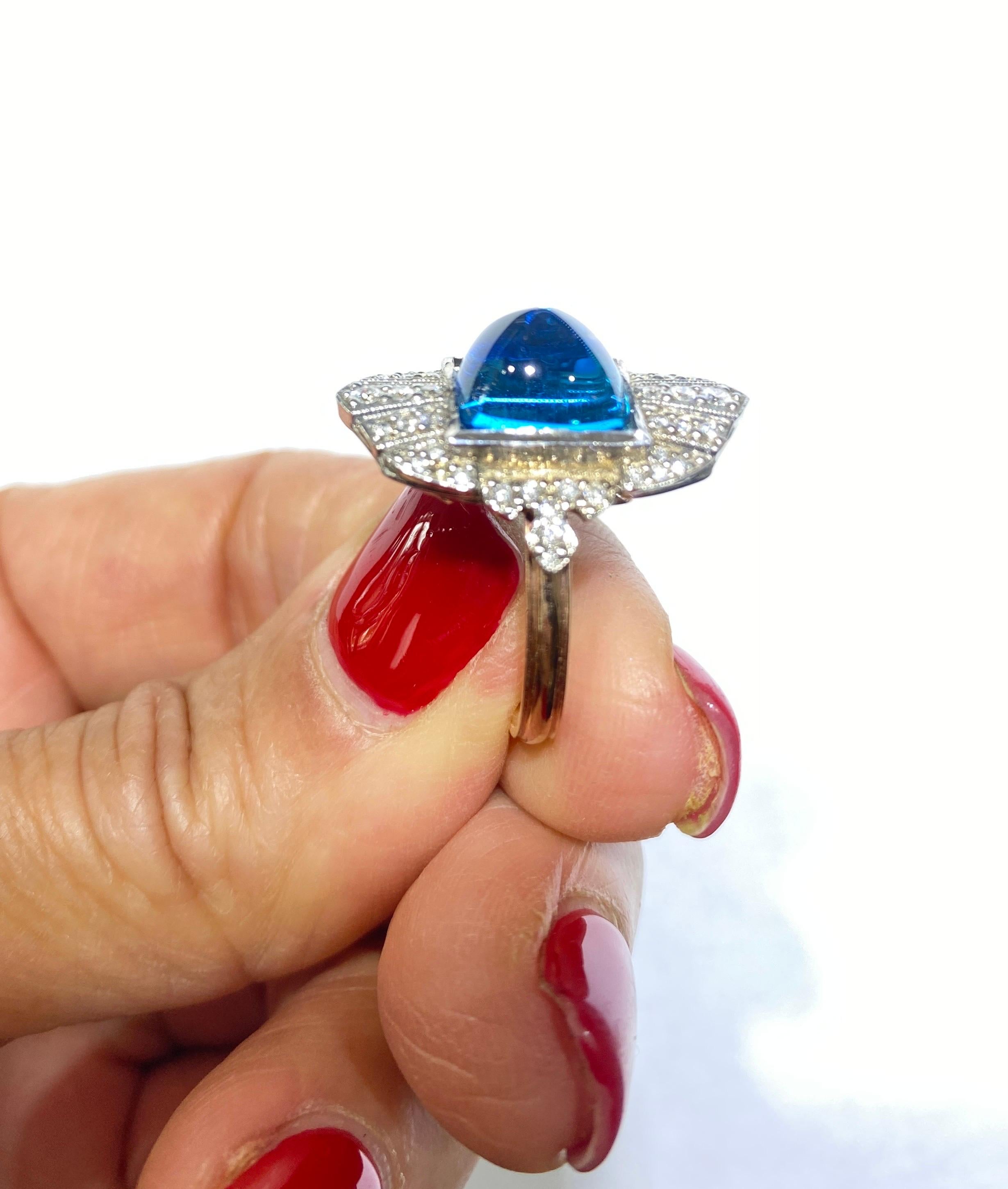 La pierre bleue de taille cabochon Sugarloaf est sertie dans un bouclier de diamants pavés. Jolie bague avec un grand style victorien et un design de galerie ouverte en dessous. Les diamants entourent les anneaux et sont sertis en pavé. Le poids