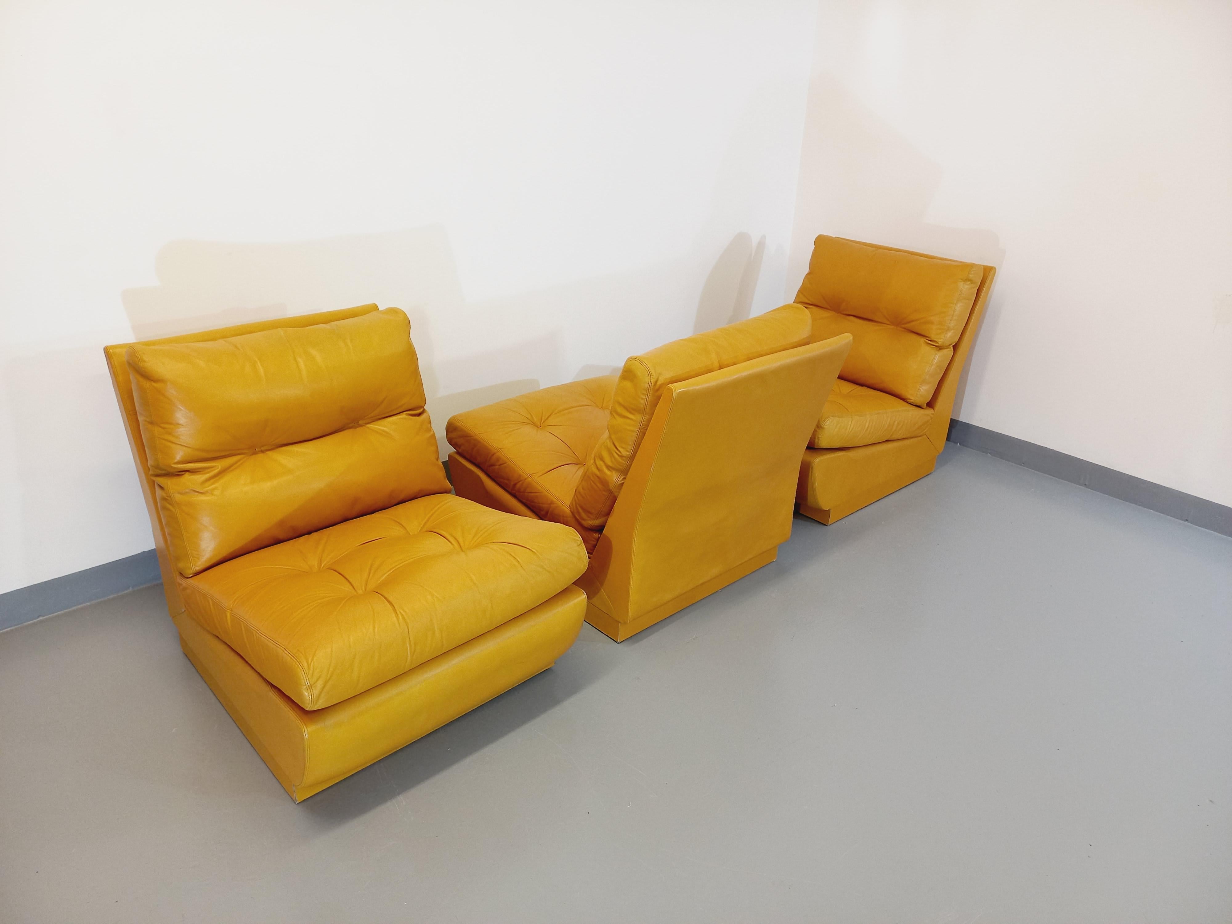3 fauteuils chauffeuses Roche Bobois vintage des années 70, dans le goût du designer français Jacques Charpentier, en cuir jaune moutarde, pouvant être utilisés séparément ou assemblés pour former un canapé, pieds invisibles réglables pour ajuster