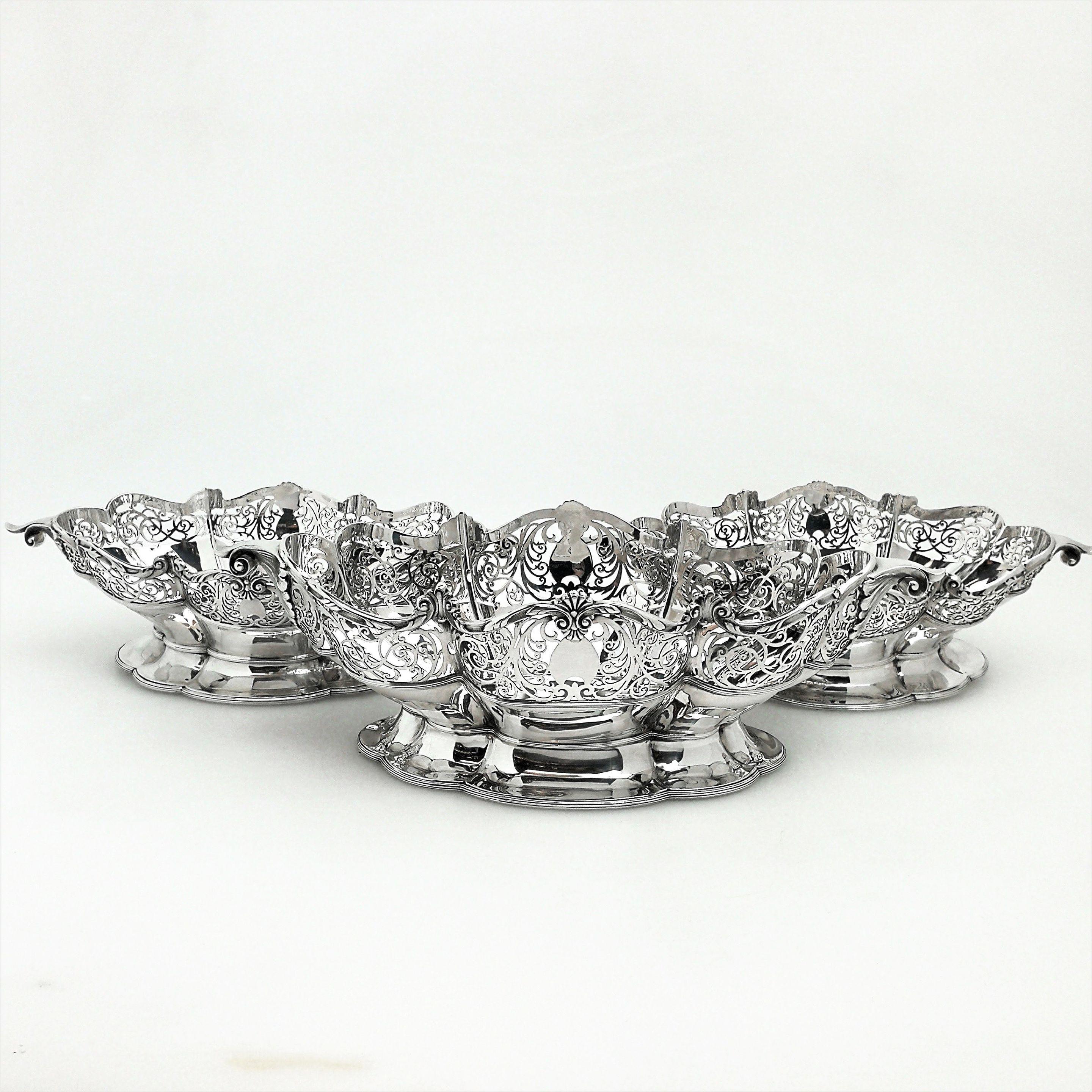 An elegant set of three solid silver baskets comprising of one large dish and a pair of smaller dishes. This set of three dishes features an delicate pierced scroll design around the rim of a shaped body. The rim has an applied band of scroll and
