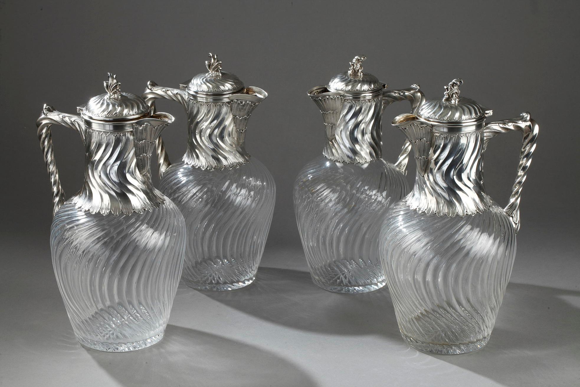 Set of four ewers in crystal cut with twisted ribs and silver mount. Every ewer has a relief wave design at the neck, a shell beak and twisted handle. The hinged lid is decorated with a flower-shaped grip.

Size of 2 ewers (1st pair)
H 22.5 cm
P