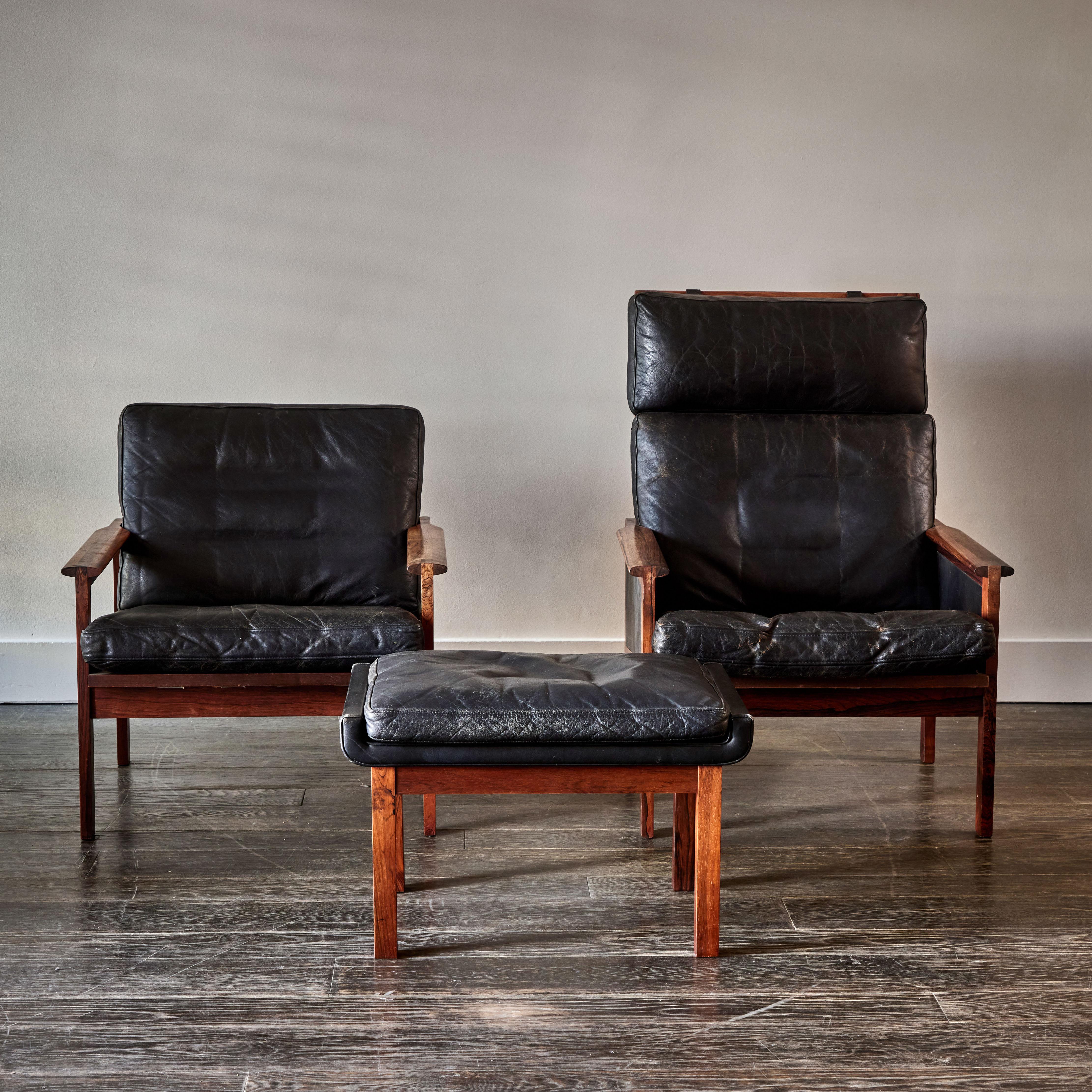 Suite of two black leather and wood Danish mid-century chairs and ottoman. Sexy and relaxed, and with excellent lines, the strong, geometric framework contrasts beautifully with the comfortable leather upholstery. 

Denmark, circa