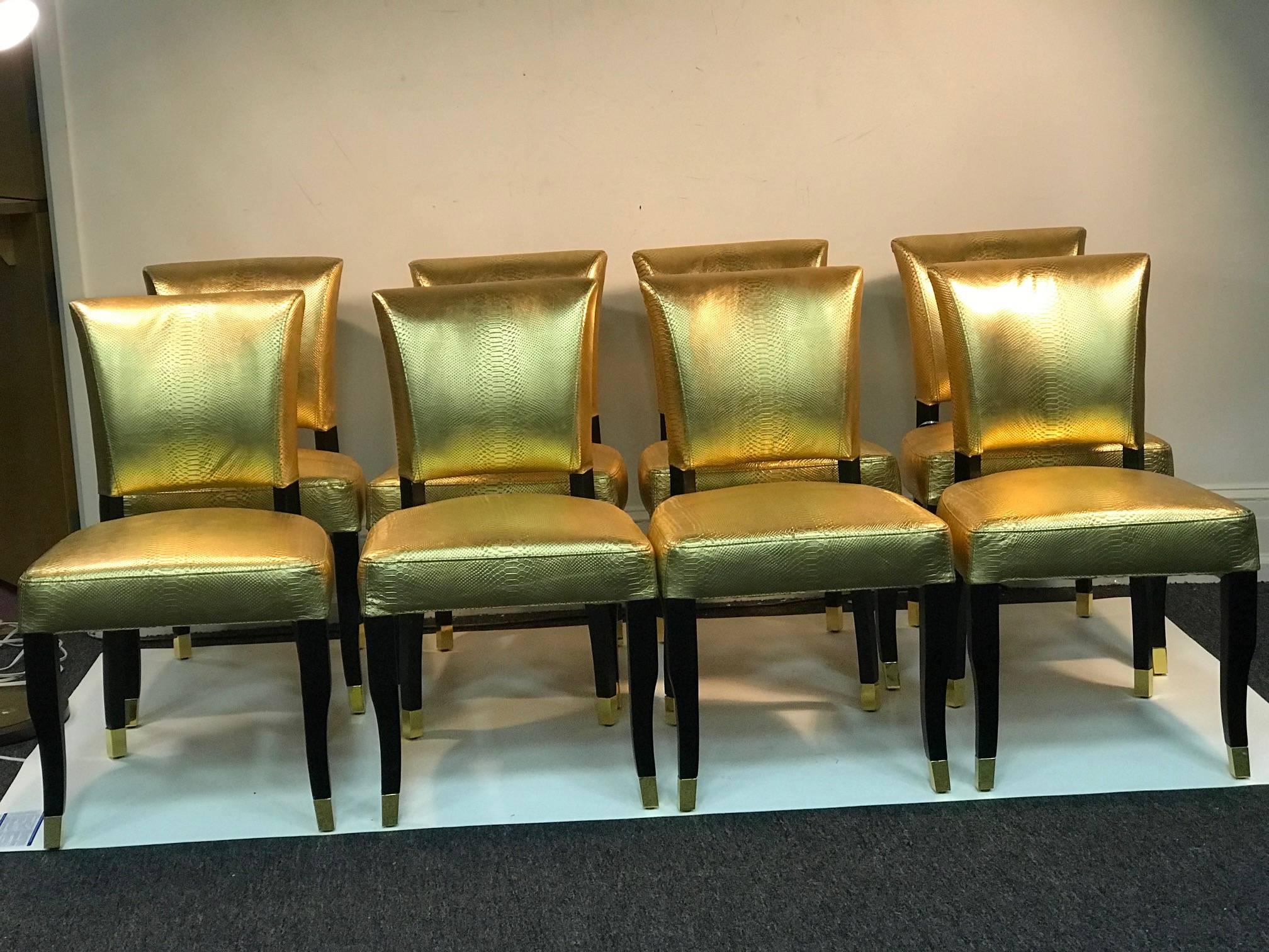 Suite of eight faux gold snakeskin dining chairs with ebonized legs and polished gold toned brass sabot legs and gold tone brass decorative buckle on their backs.