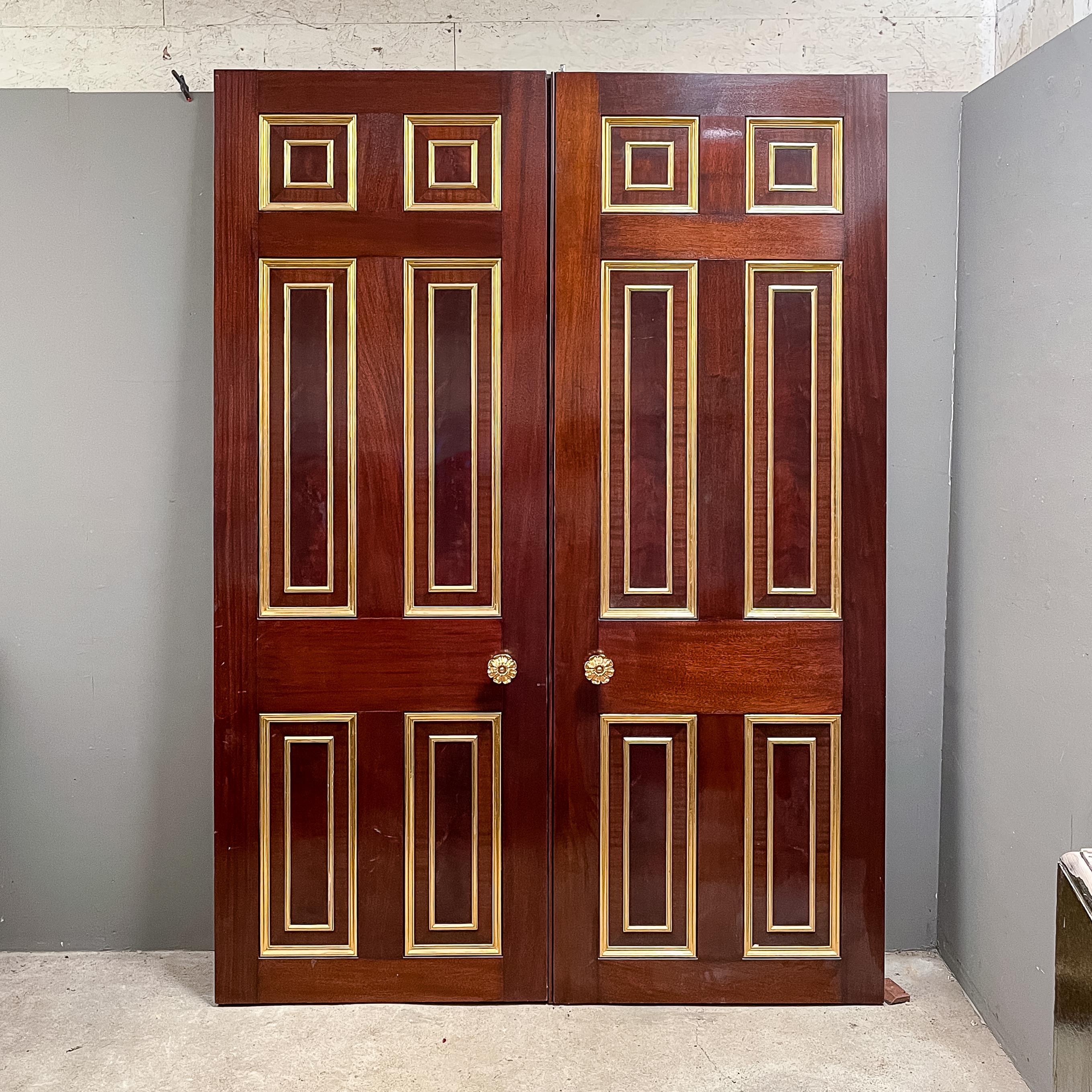 A set of English Mahogany entrance doors, each side with parcel-gilded fielded panels - a pair of square panels, above two long and two short, each side of each leaf centred with a gilt-metal flowerhead boss, the doors hung on well-specified hinges