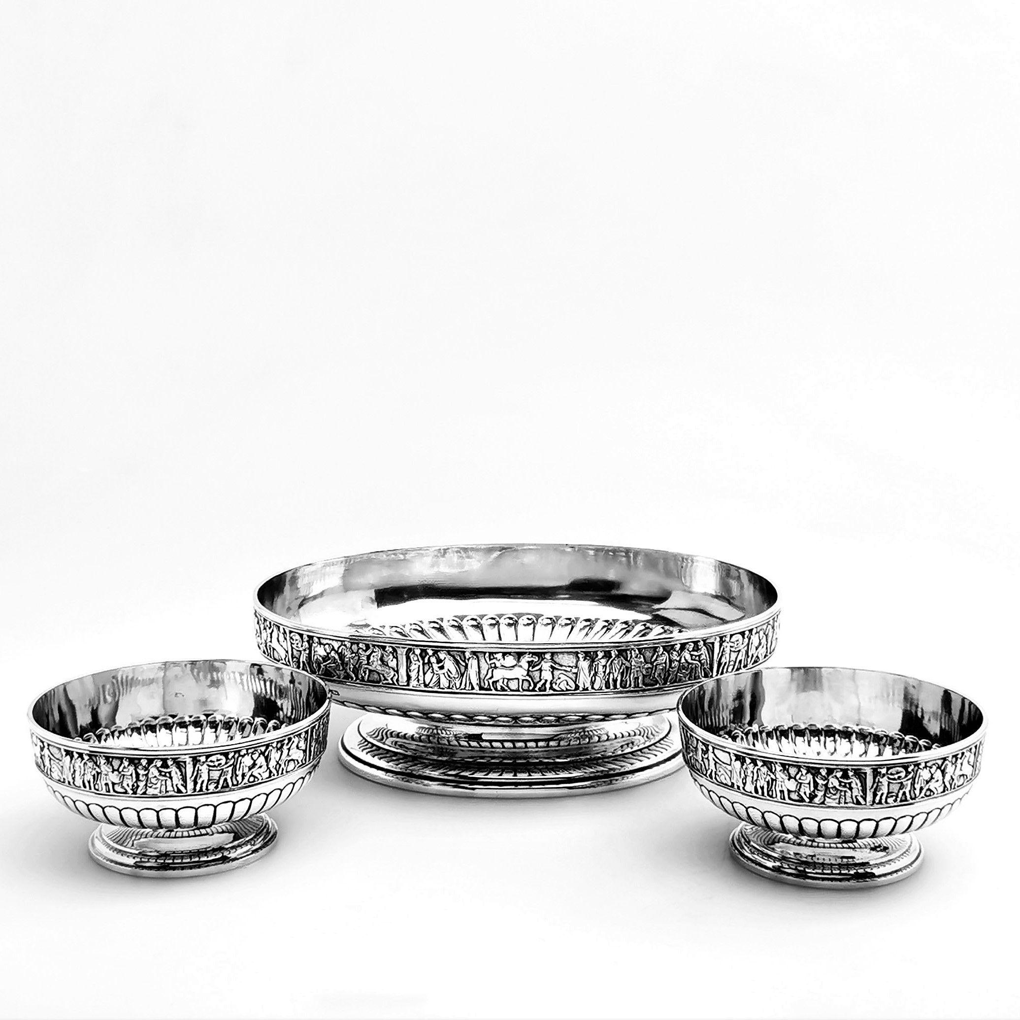 A Suite of Three beautiful Antique Victorian Silver Dishes comprising of a large oval central dish and a pair of round dishes. Each dish is decorated with a band of chased classical figures above a half fluted base. Each dish stands on a spread
