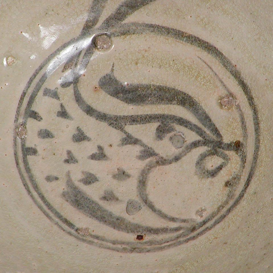 Thai Sukhothai kiln bowl with black slip painting of a fish with his tail extending beyond the concentric band on center, further band decoration at the lip and outside wall, covered overall in a crackled milky greenish white translucent glaze