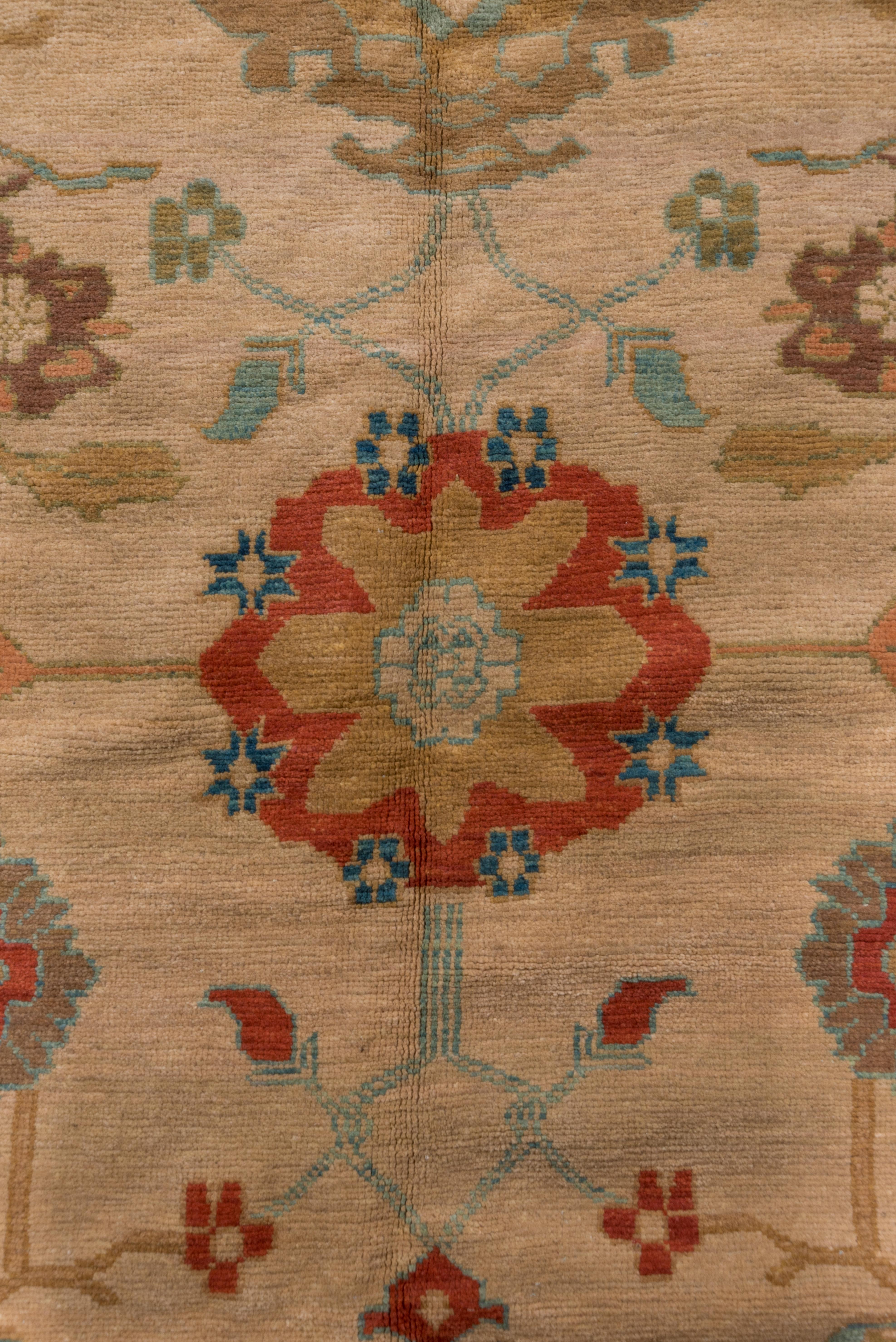 On an oatmeal ground, the pattern is organized into three columns with symmetric blue petal palmettes in a central column while leafy rosettes and winged cartouches appear in the side columns. The tonally en suite border displays rosettes and paired