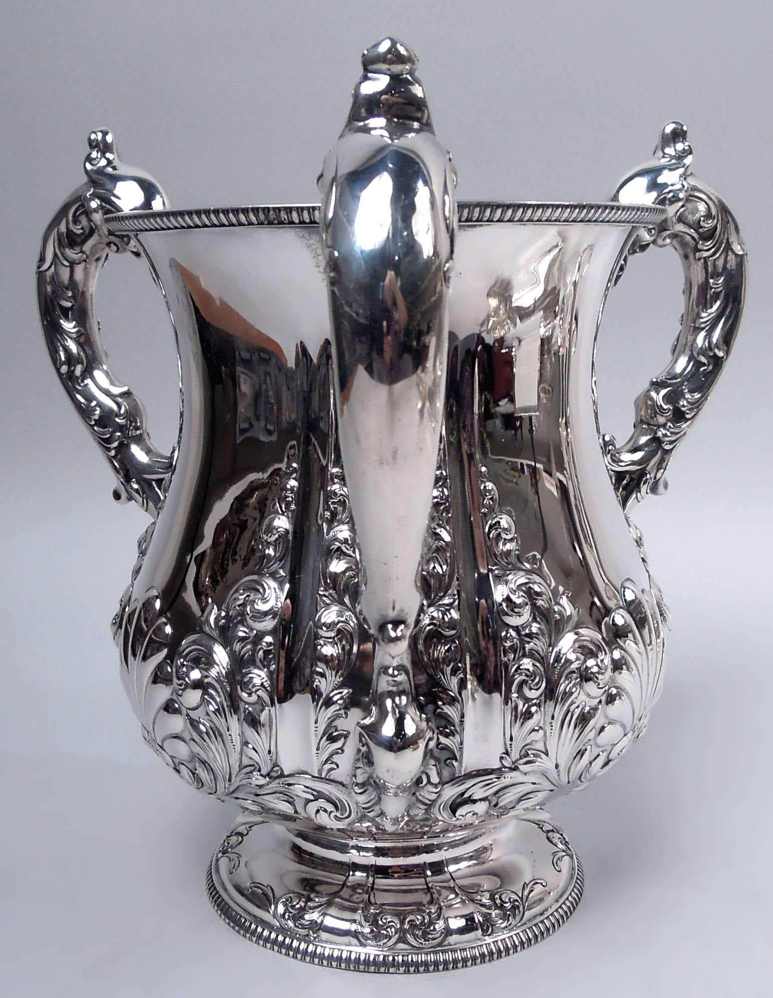 Klassische viktorianische Liebestasse aus Sterlingsilber, um 1890. Balusterschale auf erhöhtem Fuß; 3 blattumwickelte und -montierte S-Rollengriffe. Ziseliertes und geprägtes Ornament mit kühnen Muschelschalen zwischen Blattranken. Gegossene Eier-