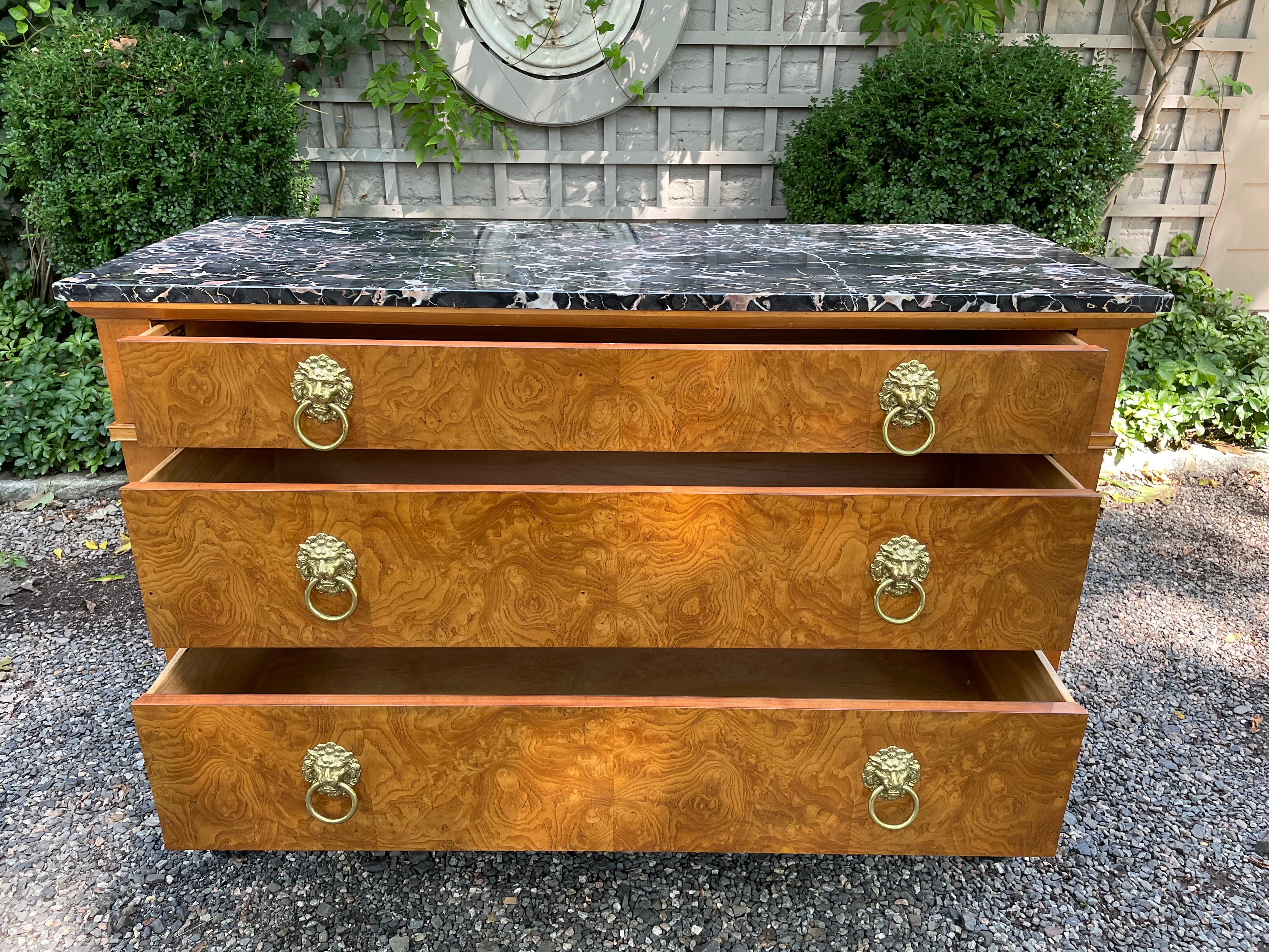 This is an exceptional vintage burlwood chest by Baker Furniture. The top is made of a 2” thick piece of black marble with lively veining. The chest has three drawers with the original lion’s head hardware in brass. Sexy ebonized lion paw feet