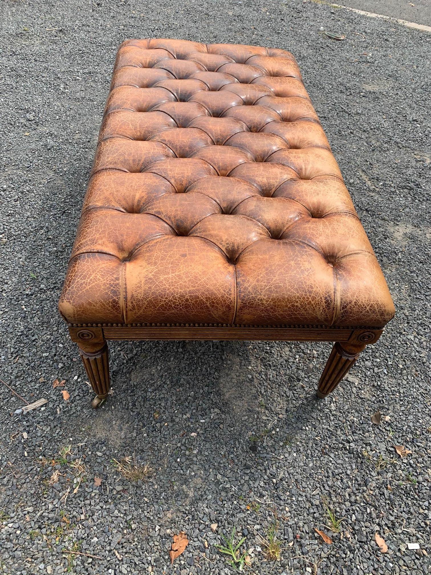 A hard to find handsome English 19th century tufted leather ottoman with brass nailhead details. The carved mahogany base includes reeded tapered legs that terminate in brass casters.
   