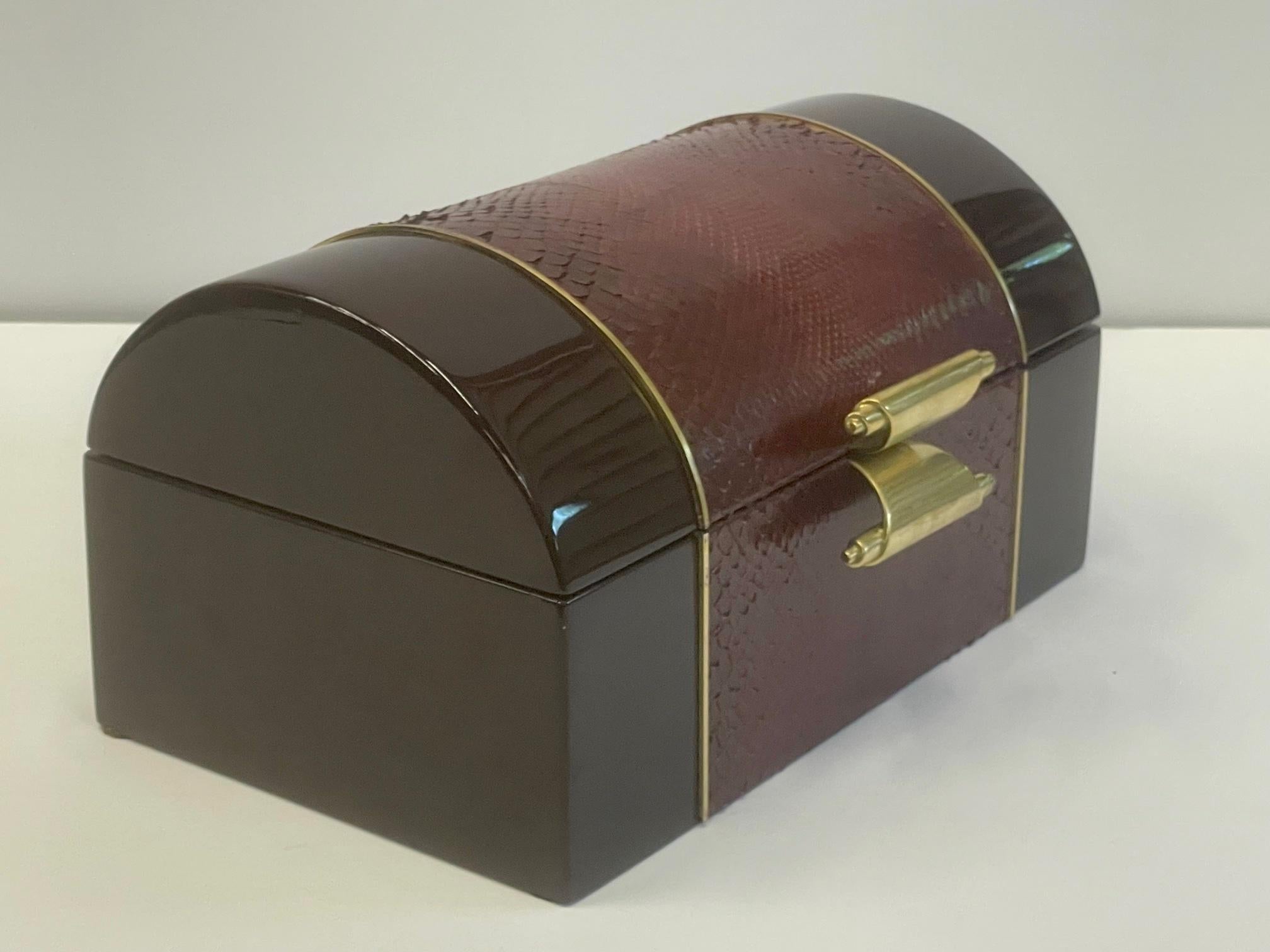Sumptuous Italian treasure chest shaped box having high gloss dark maroon laquer exterior decorated with a lighter shade of maroon faux snakeskin and brass. Interior is lined in velvet.