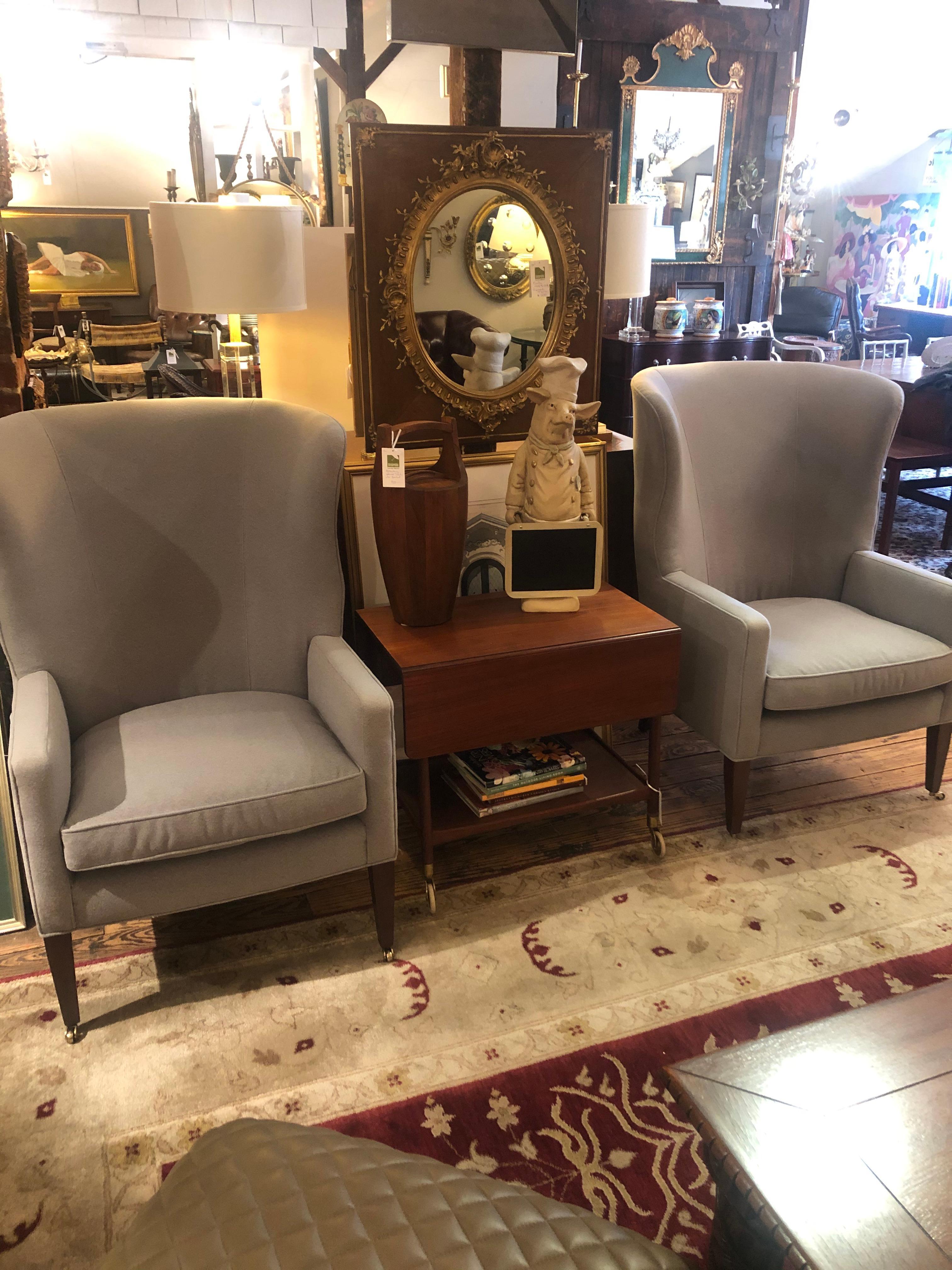 Absolutely sublime pair of barrel back wing chairs newly upholstered in a soft refined grey flannel. The legs are mahogany, the back legs splay out slightly in a lovely shape, and all terminate in brass casters.. Super comfy.