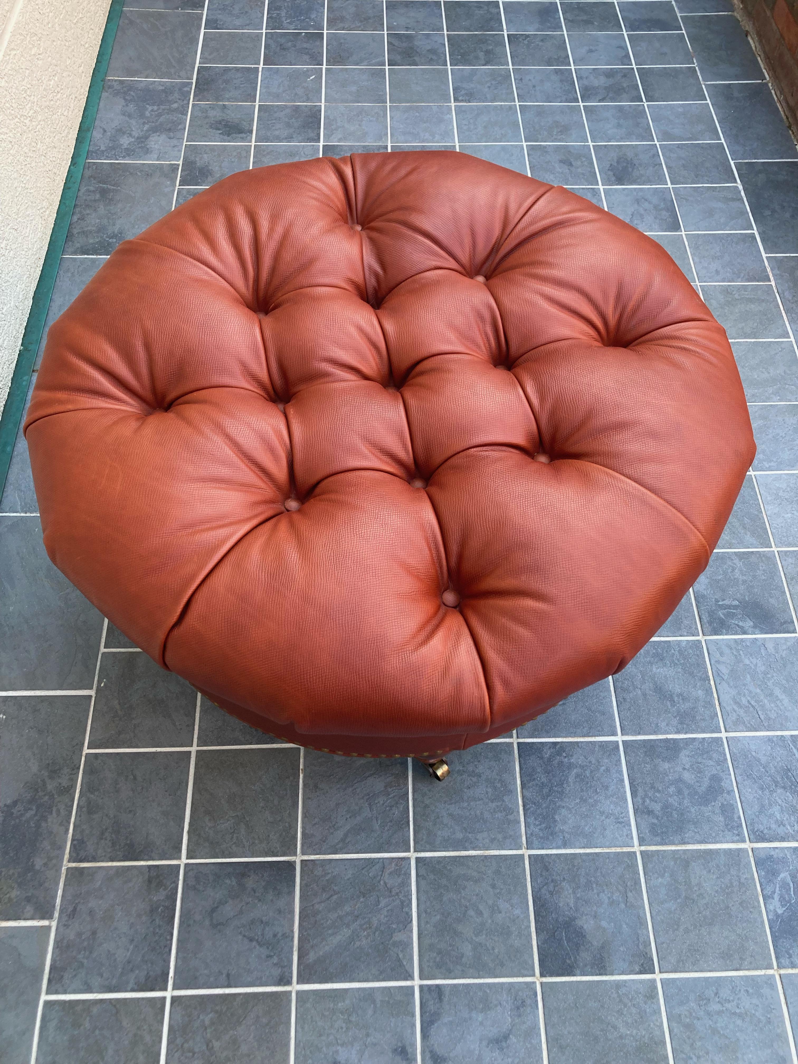 Striking Edward Ferrell and Lewis Mittman tufted terracotta red textured leather round coffee table ottoman having turned mahogany feet terminating in brass casters. Brass nailheads are a handsome finishing touch. This was custom purchased through a