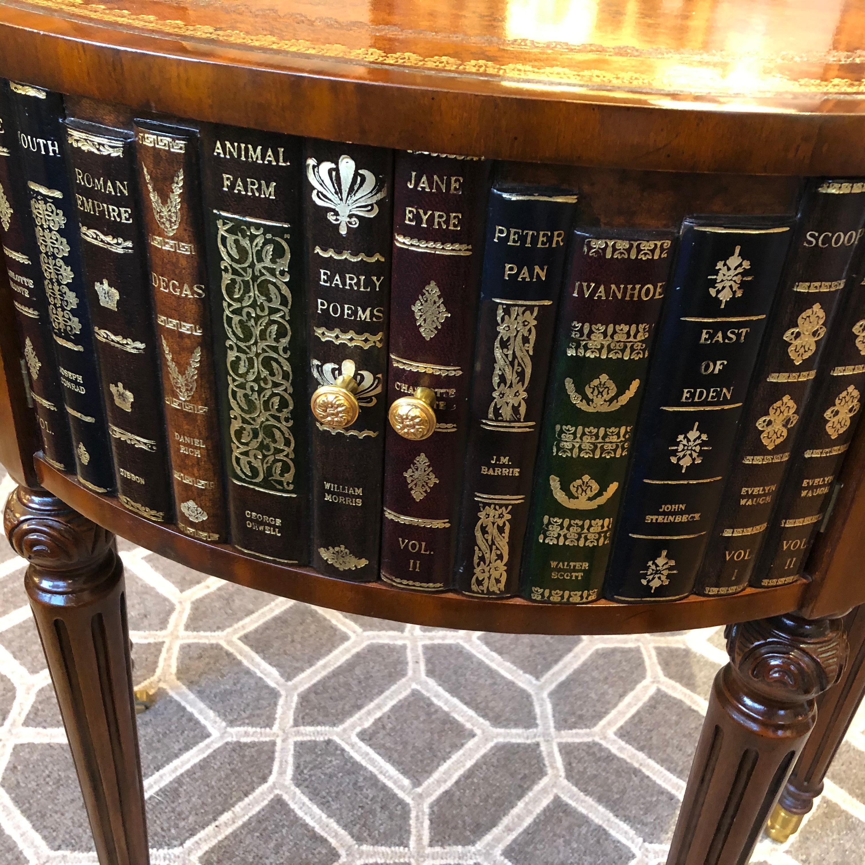 Handsome leather wrapped center table or side table having tooled leather top and trompe l'oeil books around the periphery. There are 3 sets of double doors that open to storage, and 3 sets of 2 drawers. Mahogany legs are carved and terminate in