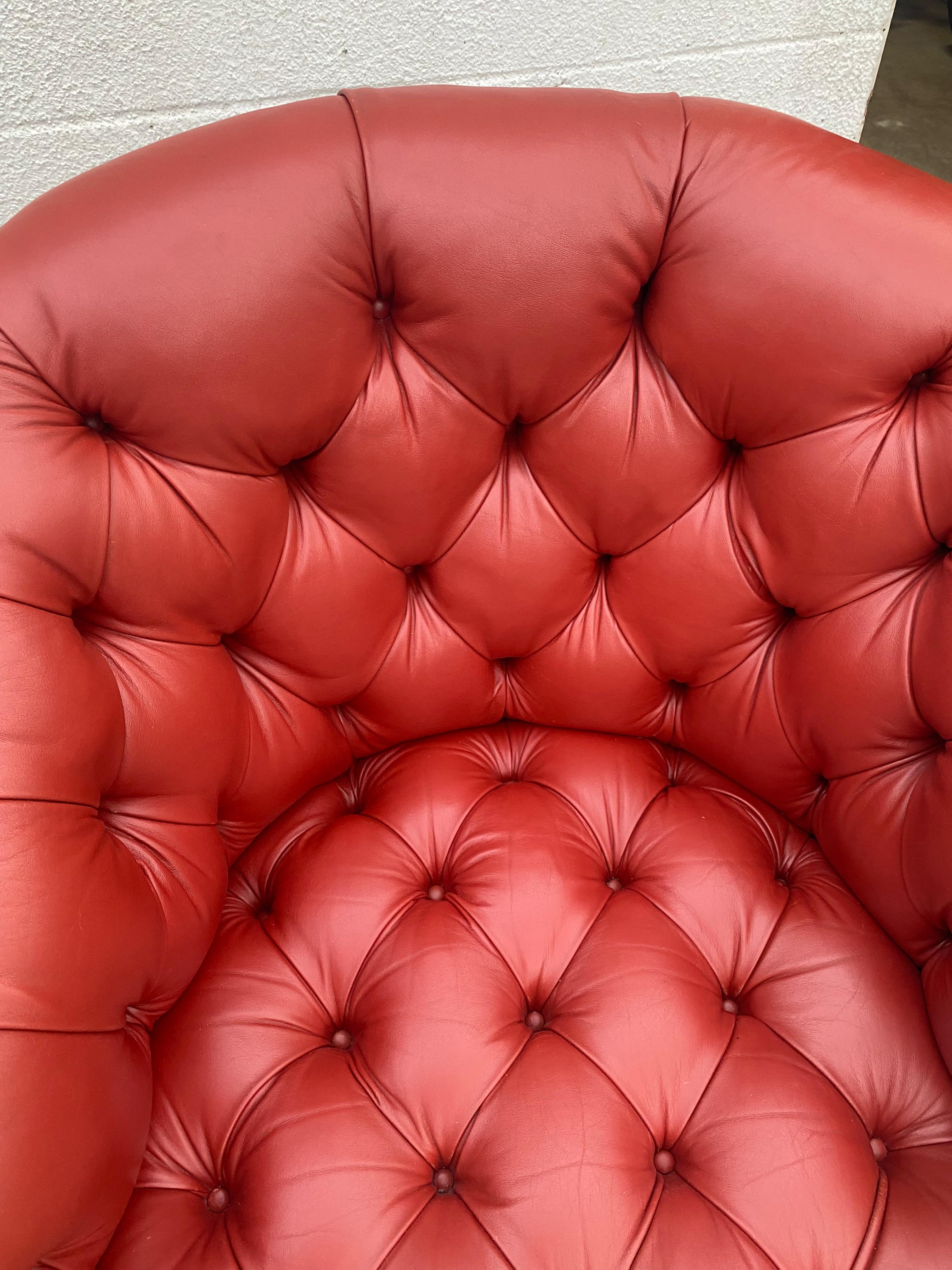 Luxurious pair of barrel back swivel club chairs with deep button tufting and soft muted brick red leather upholstery.  Even the swivel underneath is leather clad.
