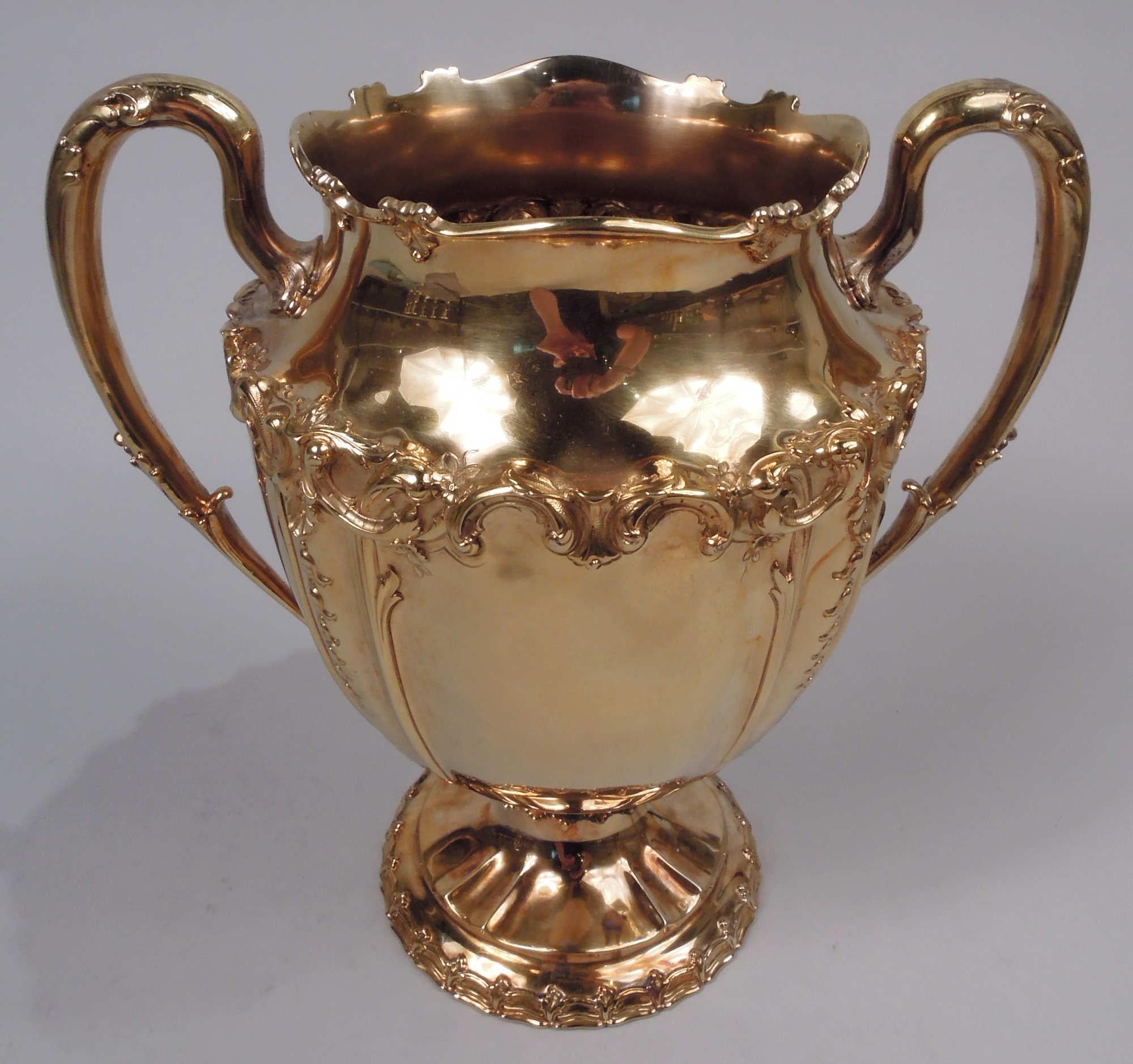 Edwardian Classical sterling silver urn. Made by Tiffany & Co. in New York. Curved and tapering bowl with leaf flange on domed foot; leaf-capped, wrapped, and mounted high-looping side handles. Chased leafing-scroll border with pendant flowers.