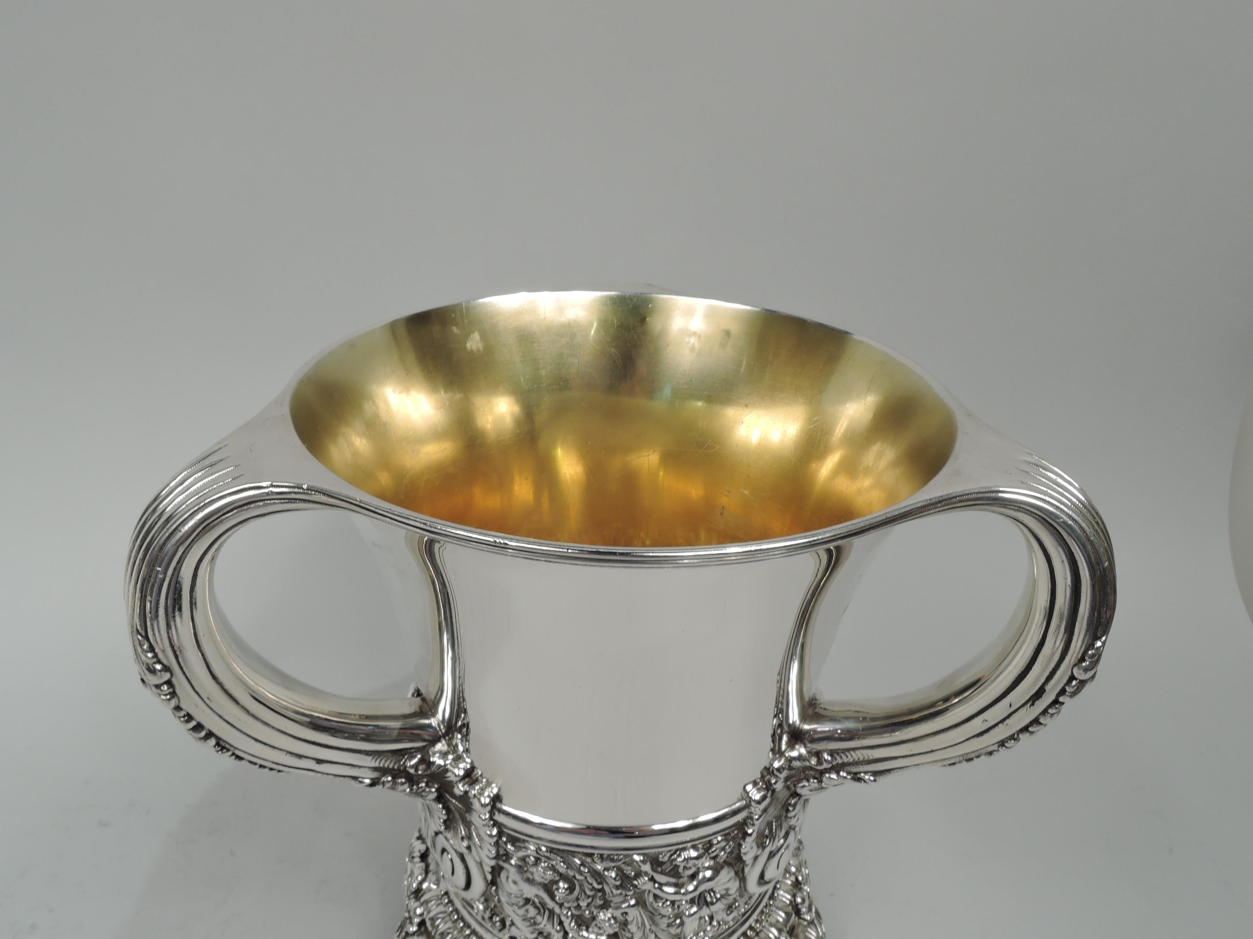 Olympian sterling silver wine cooler. Made by Tiffany & Co. in New York. Each: Round with gently tapering sides and three reeded c-scroll handles with leaf mounts and caps. Foot ring with beading and bead-and-reel ornament, and 3 paw supports with
