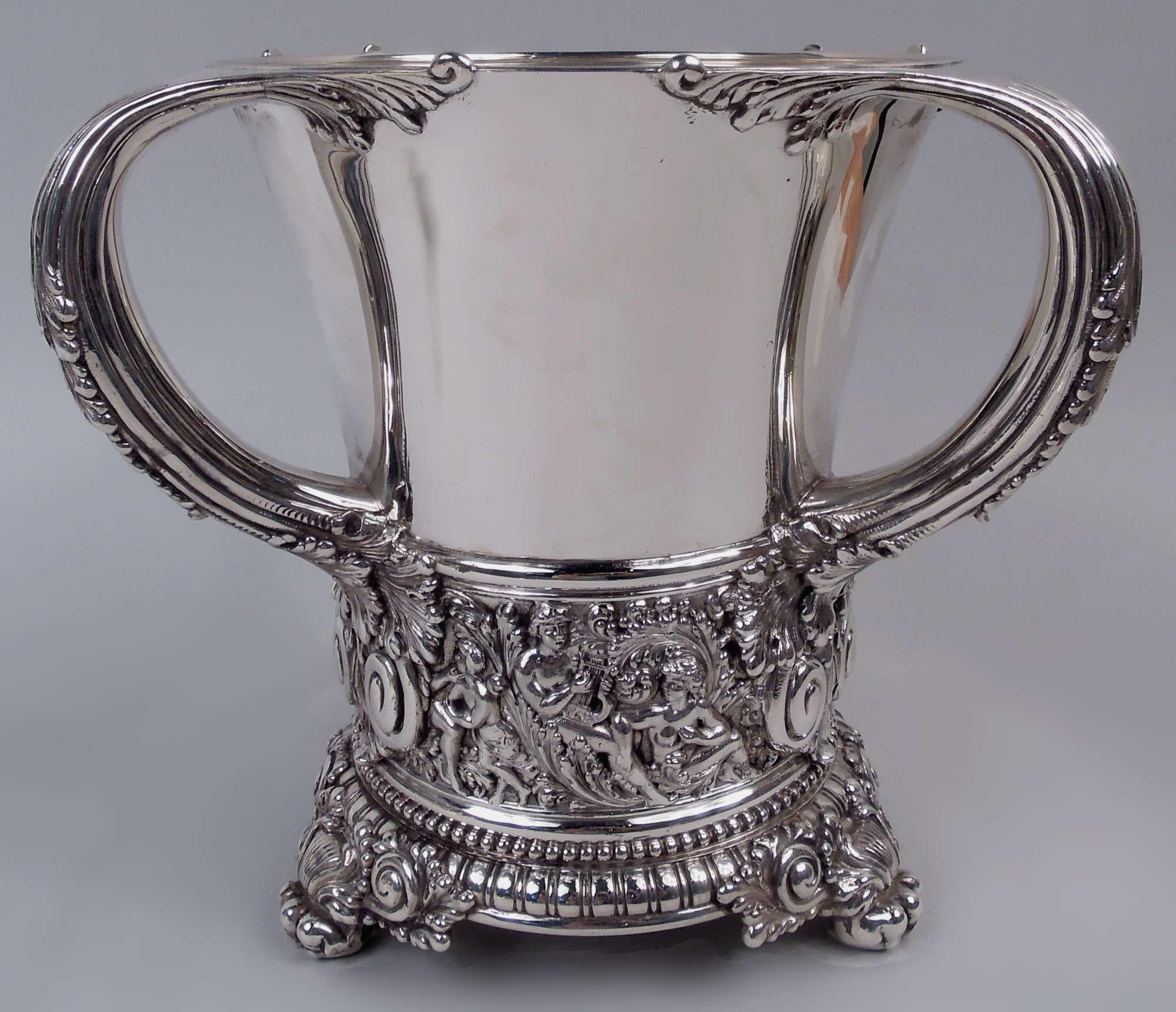Olympian sterling silver wine cooler. Made by Tiffany & Co. in New York. Round with gently tapering sides and three reeded c-scroll handles with leaf mounts and caps. Foot ring with beading and bead-and-reel borders, and 3 paw supports with leafy