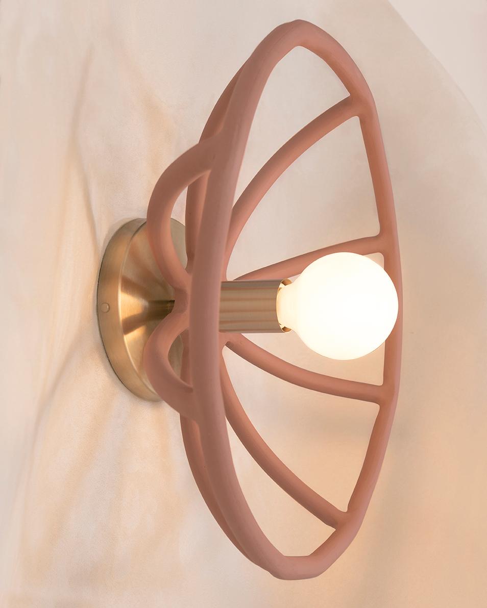 The hand-built ceramic coils cast a dramatic sunburst pattern. The terracotta coils and brass backplate adds warmth, while the glow is punctuated by the exposed light bulb, referencing the rays of light that radiate from the sun.

Material:
