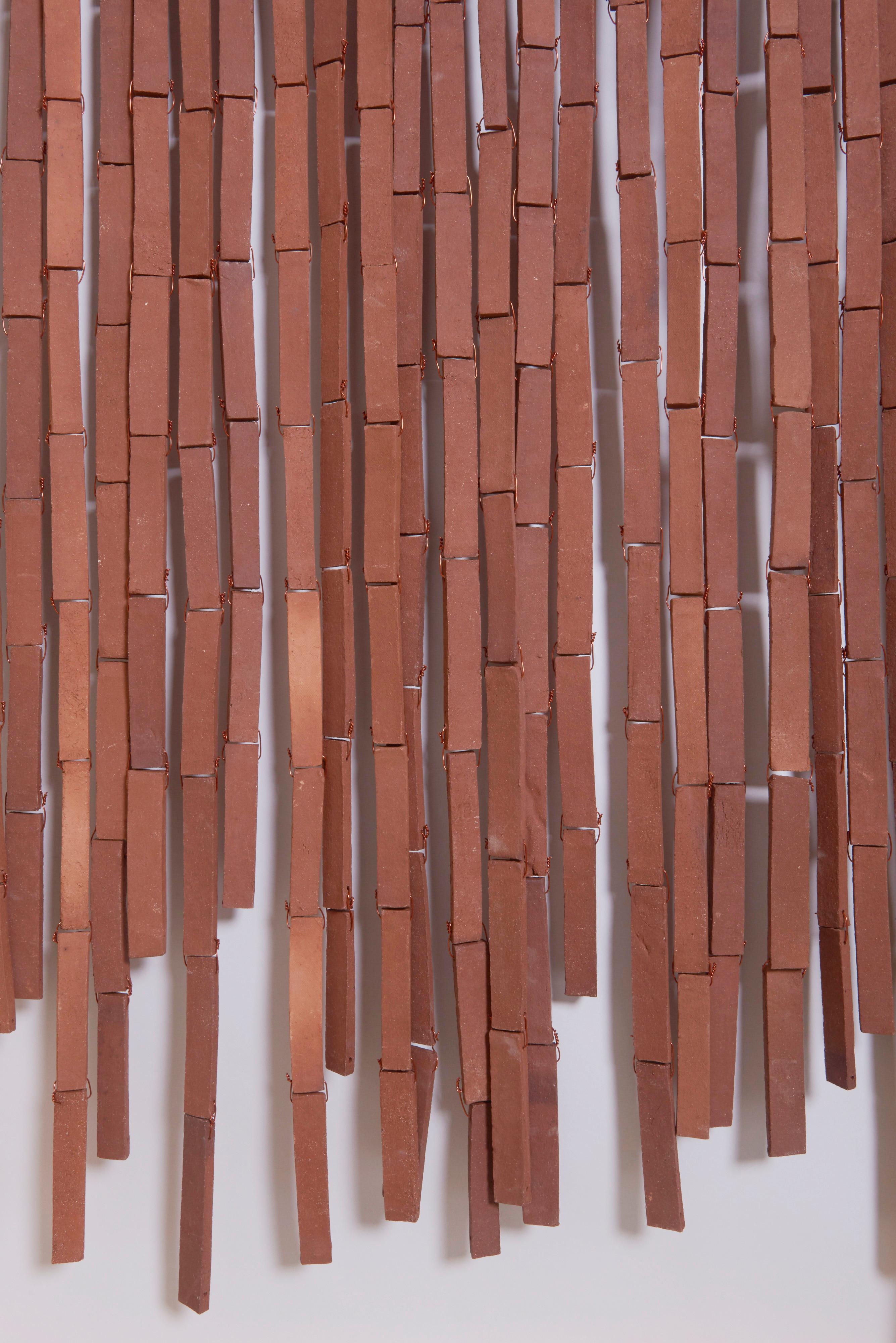 Stan Bitters sun screen made from strips of fired unglazed clay. Each strip is approximately 2 cm / 0.8 inch wide and they vary in length. The individual pieces are joined by copper wire. Chiming occurs when the unattached ends strike one another in