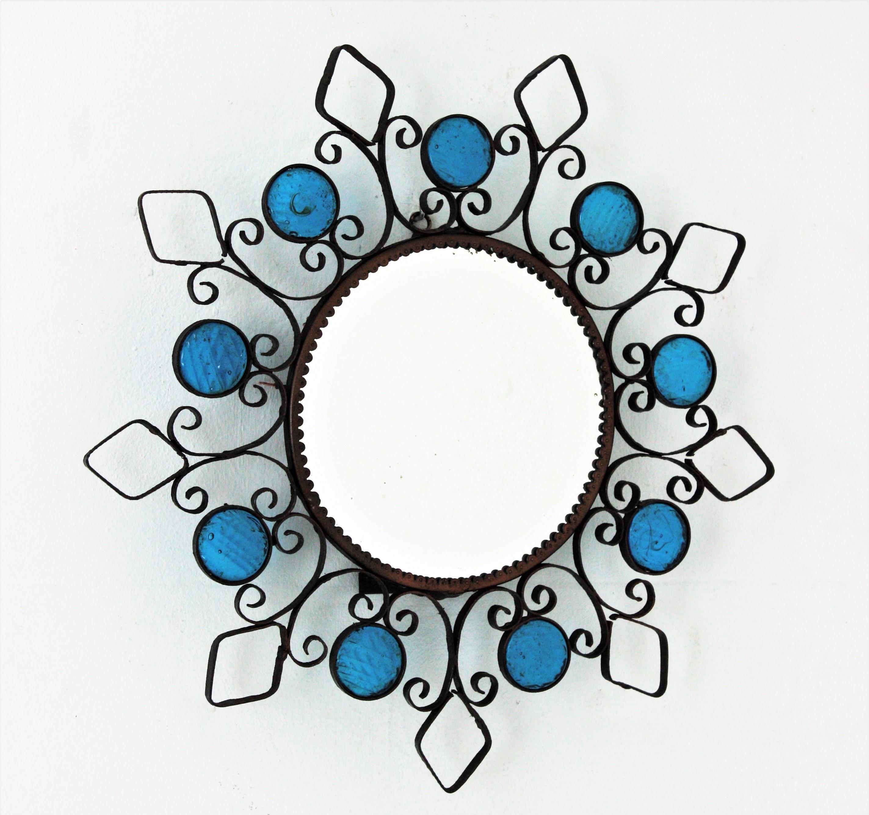 Beautiful wrought iron backlit sunburst mirror accented by blue glass circles, Spain, 1950s.
This backlit wall mirror features a wrought iron frame with scrolled details, rhombus and circles adorned by small pieces of textured blue glass.
It can