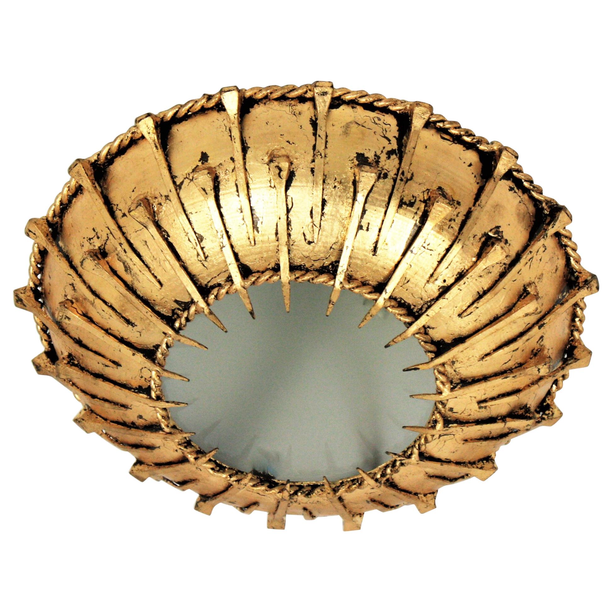 A Brutalist gilt wrought iron sunburst flushmount or light fixture from the Brutalist period, France, 1950s.
It has a frosted glass diffuser in the centre and a double layer of iron nails decoration. It was finished with gold leaf gilding and it