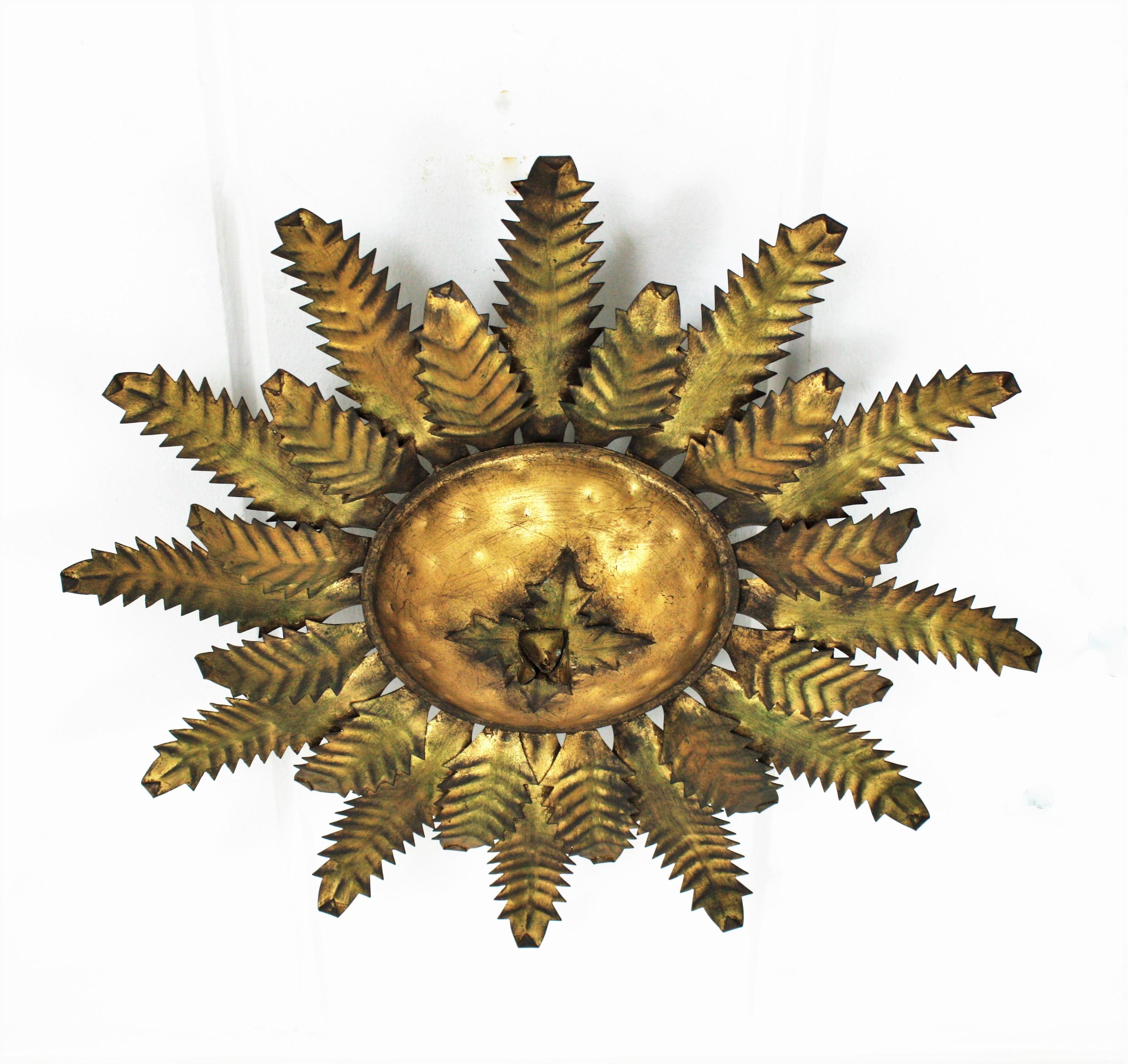 Gold leaf gilt hand-hammered iron sunburst light fixture from the Brutalist period. Spain, 1950s.
Richly decorated with the hammer marks at the central sphere. Two layers of alternating short and long scalloped leaves and a central floral foliage