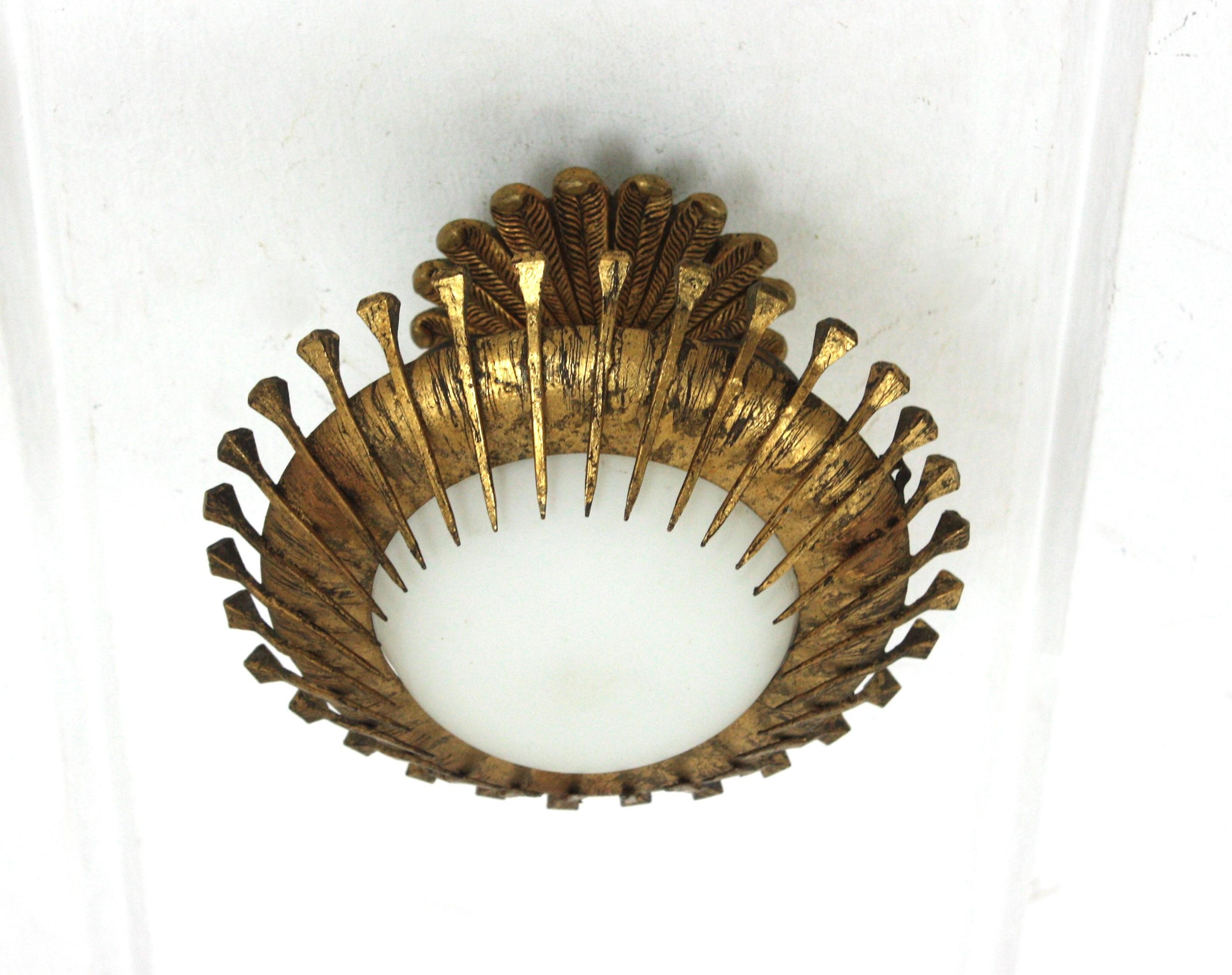 Mini-Sonnenschliff-Leuchte / Unterputzmontage, vergoldetes Eisen, Milchglas, Blattgold. Spanien, 1950er Jahre
Brutalistische Deckenleuchte aus vergoldetem Eisen mit Nägeln und einem Baldachin aus bronzenem Laubwerk.
Diese kleine Sunburst-Leuchte ist