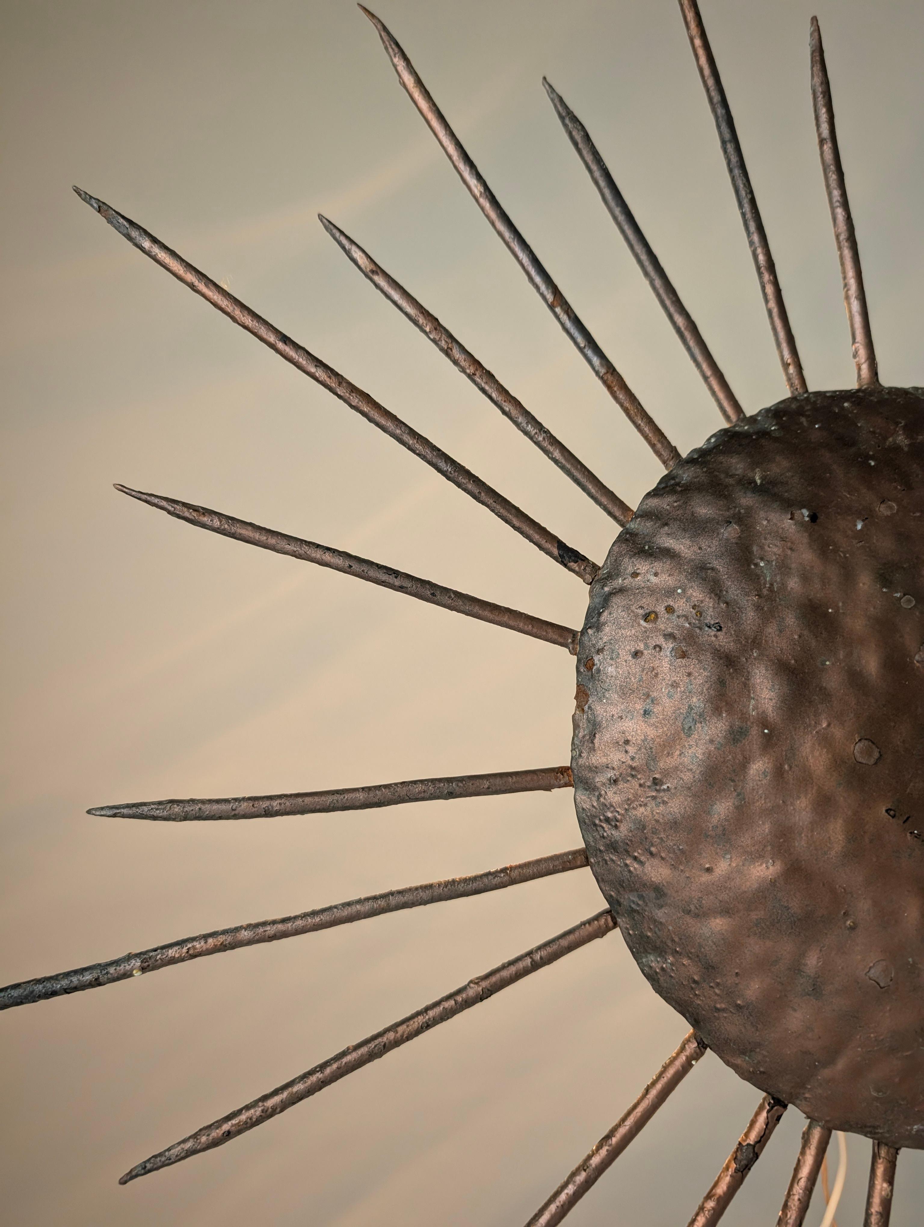 La lámpara de techo Sunburst de los años 50 está fabricada en hierro con un acabado de cobre dorado aplicado a mano. Su diseño radiante, con rayos de hierro que emulan las ráfagas de sol, es un sello distintivo del estilo moderno de mediados de