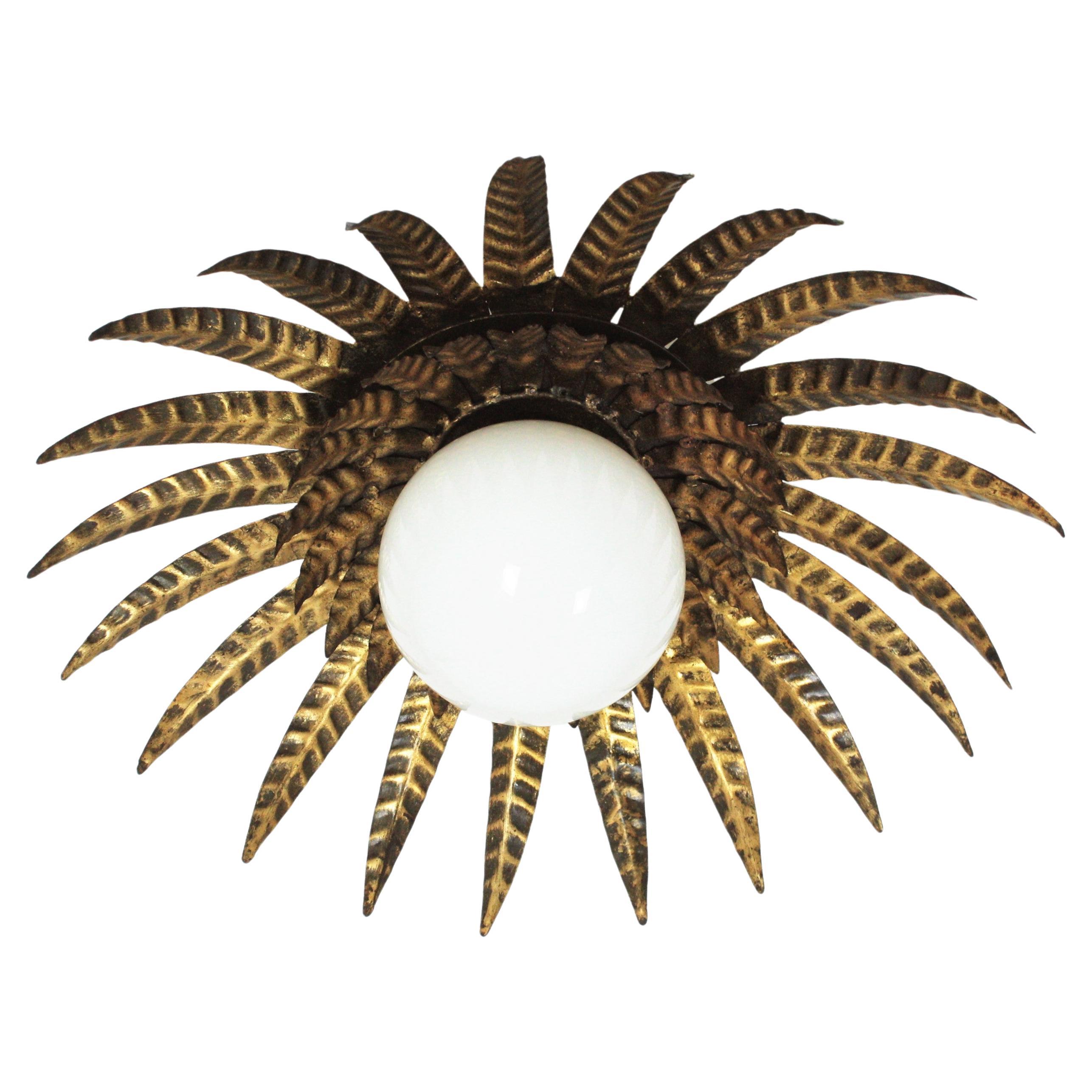 Gorgeous Brutalist gilt iron sunburst flush mount with opaline glass globe, France, 1950s.
This sunburst light fixture features a double layer of leaves / rays surrounding a central milk glass globe shade.
This ceiling flush mount combines