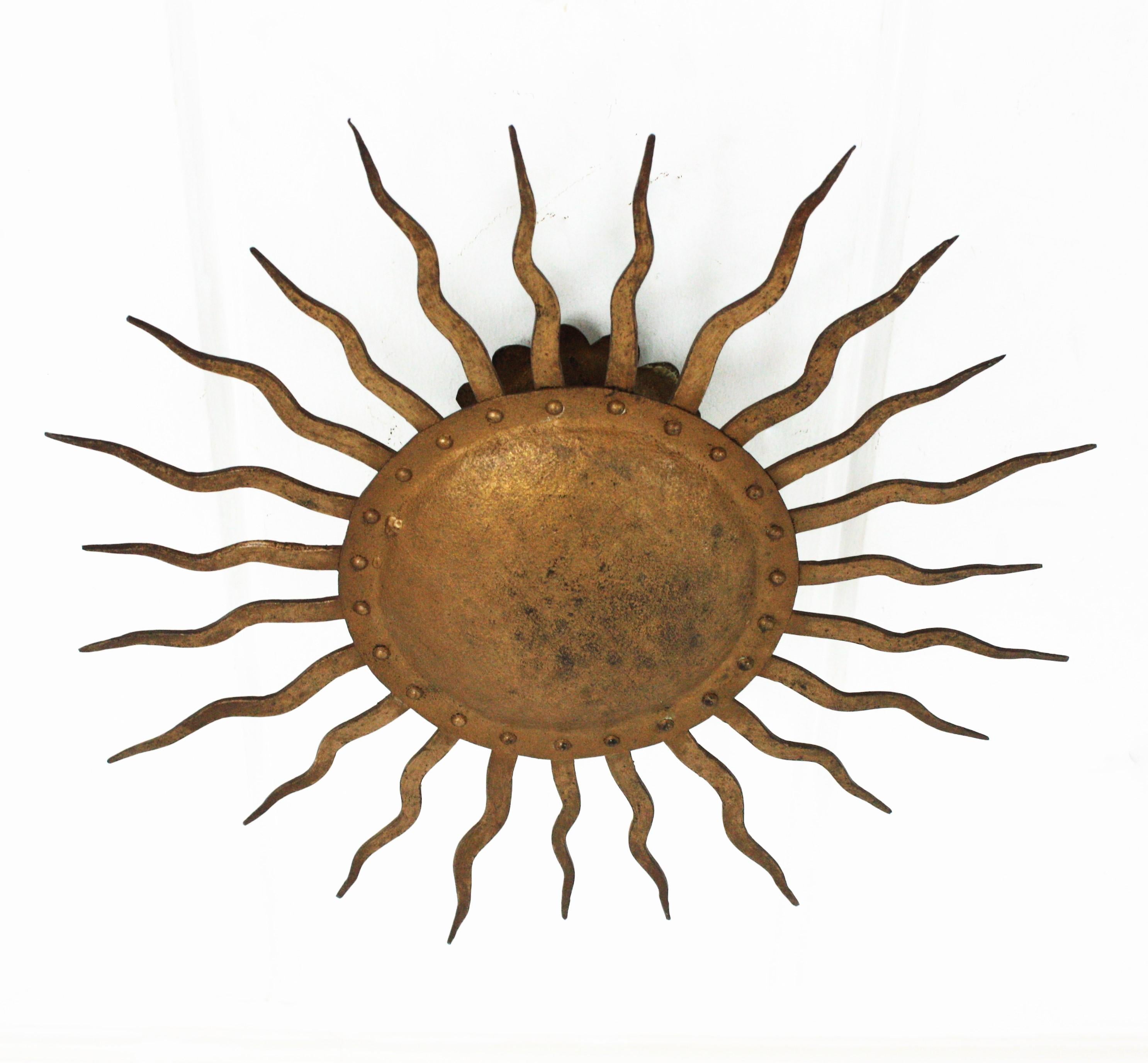 Wrought gilt hand forged iron sunburst flushmount ceiling lamp or light fixture. France, 1950s.
This brutalist style light fixture has a design Inspired in Gilbert Poillerat pieces.
This hand-hammered iron flush mount has alternating rays in two