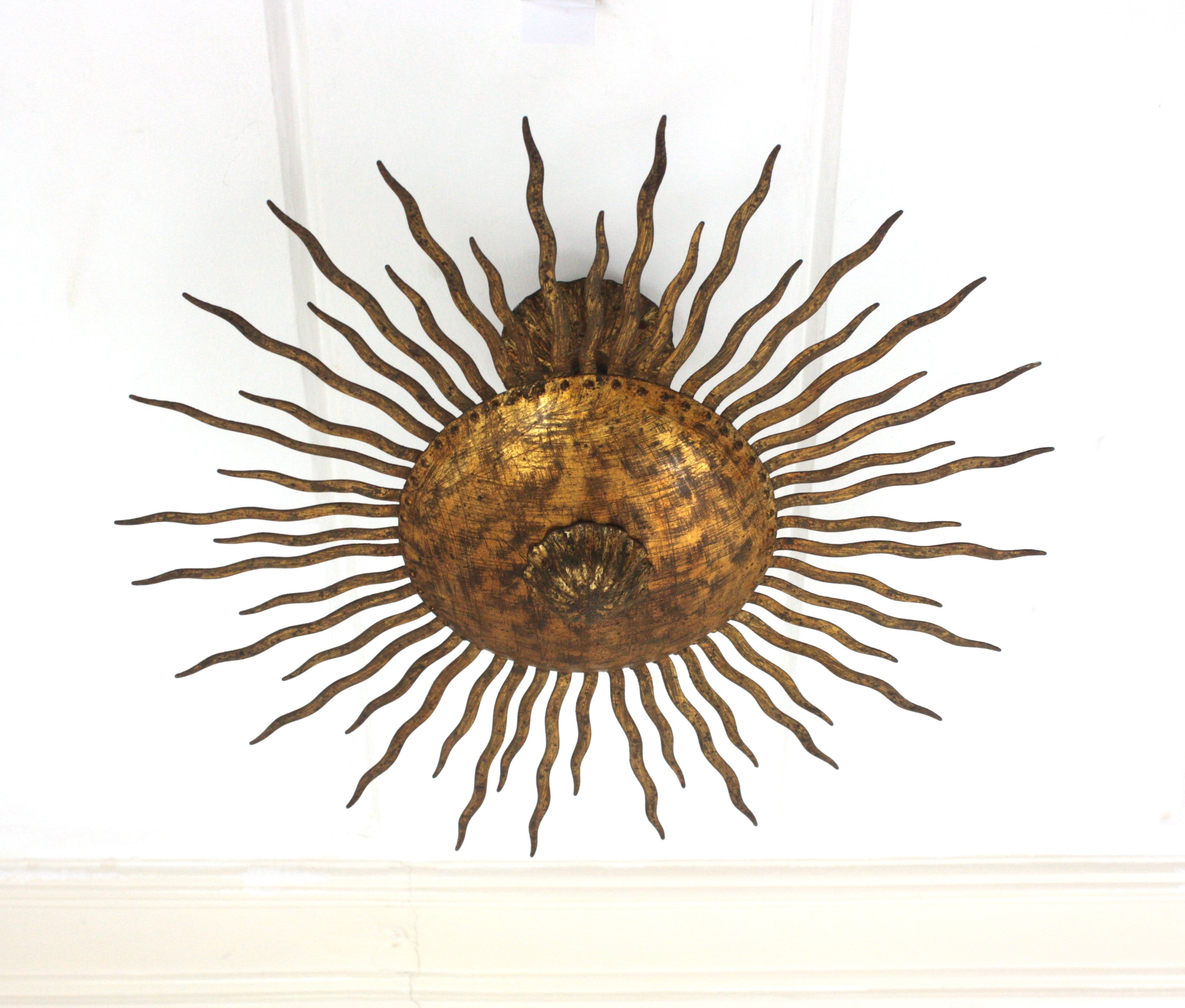 French lwrought gilt hand forged iron sunburst flush mount / ceiling light fixture. France, 1950s.
This hand-hammered iron flushmount has alternating rays in two sizes surrounding the central sphere and a flower decoration at the central part.