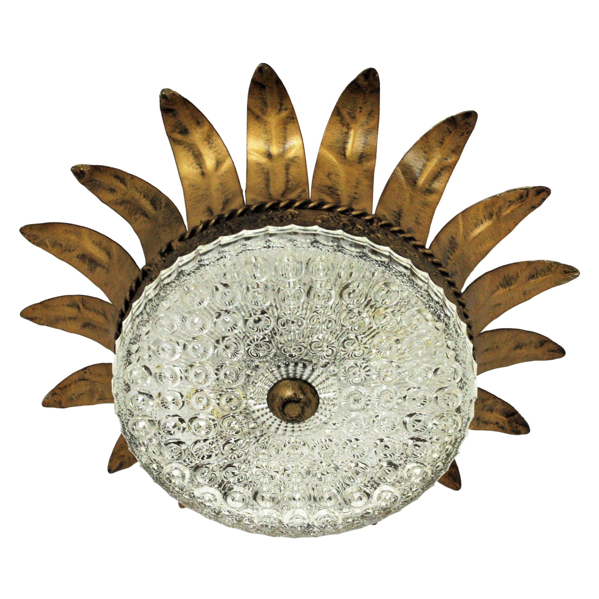 Eye-catching neoclassical style sunburst ceiling light fixture from the Mid-Century Modern period, Spain, 1950s.
This ceiling fixture features a gilt metal sunburst crown shaped structure with a pressed glass shade with a gilt iron finial.
It has