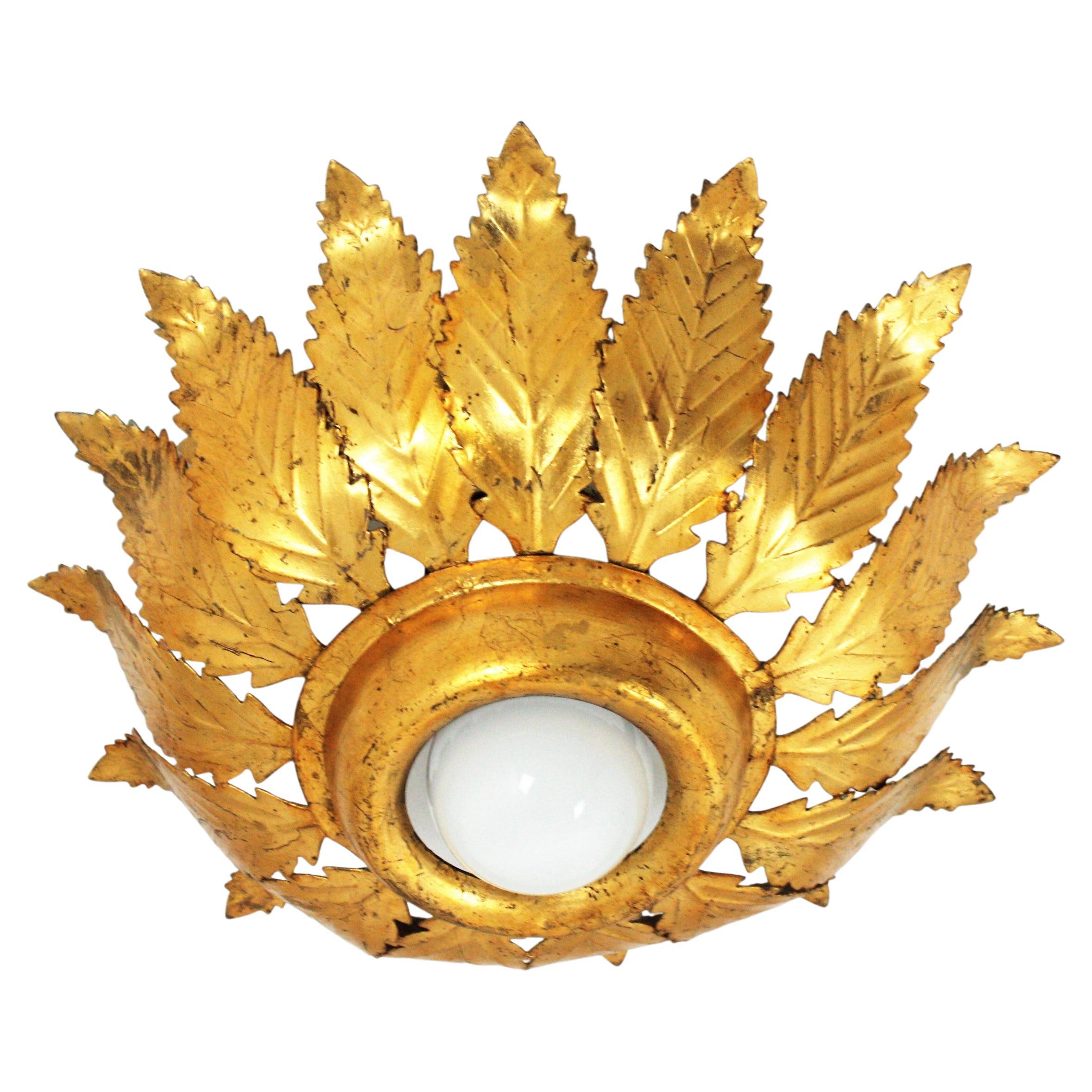 Foliage Sunburst flush mount light, iron, gold leaf, Spain, 1950s
This gorgeous spanish sunburst or crown ceiling lamp features gold leaf gilt iron leaves surrounding a central exposed bulb. It has a nice patina showing its original gold leaf