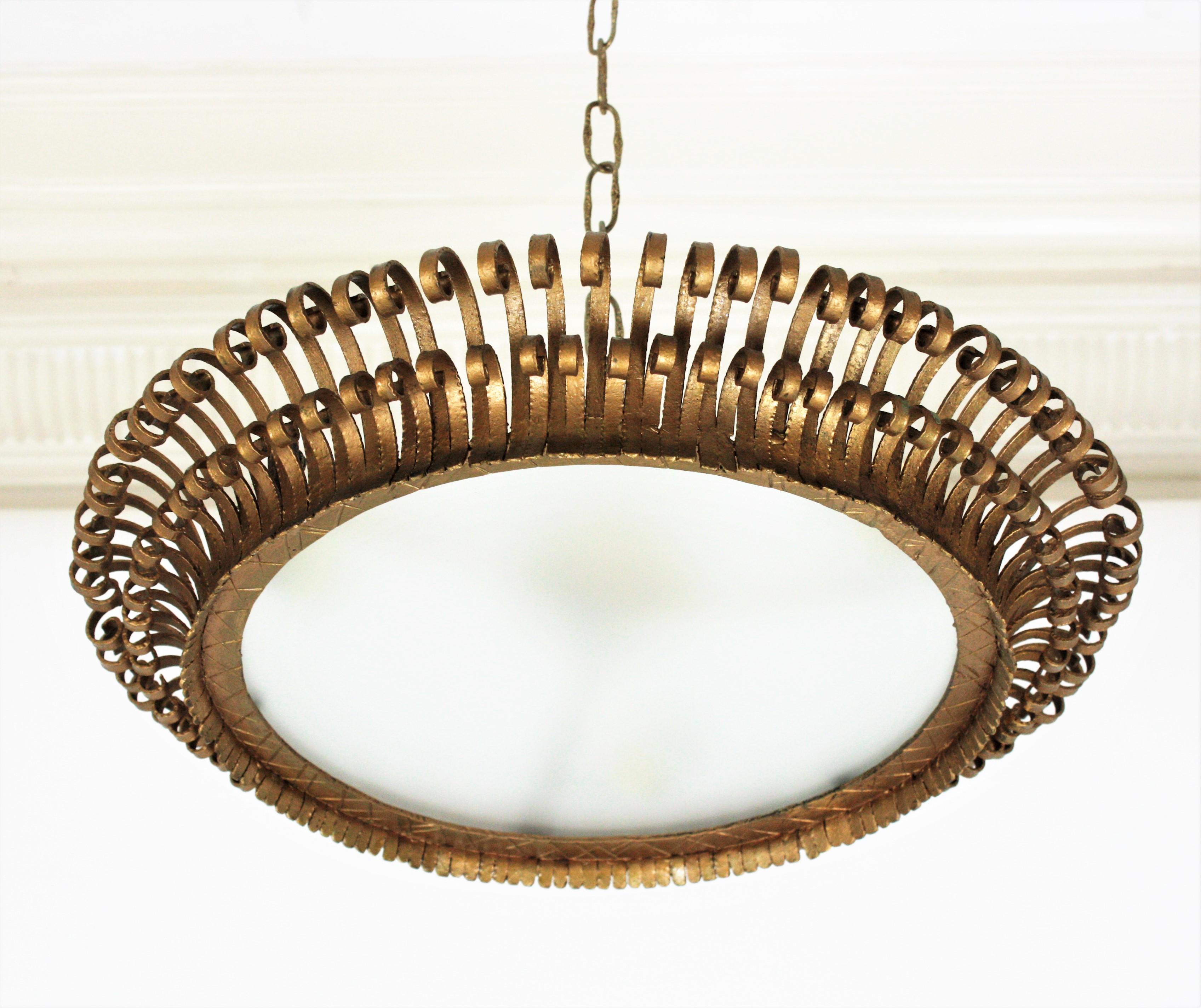Eye-catching double layered gilt iron sunburst round flushmount with eyelash scroll endings. Spain, 1950s
The frame is made by a double layer of curved beams with scrolled endings. The frosted glass diffuser allows to disperse a good amount of