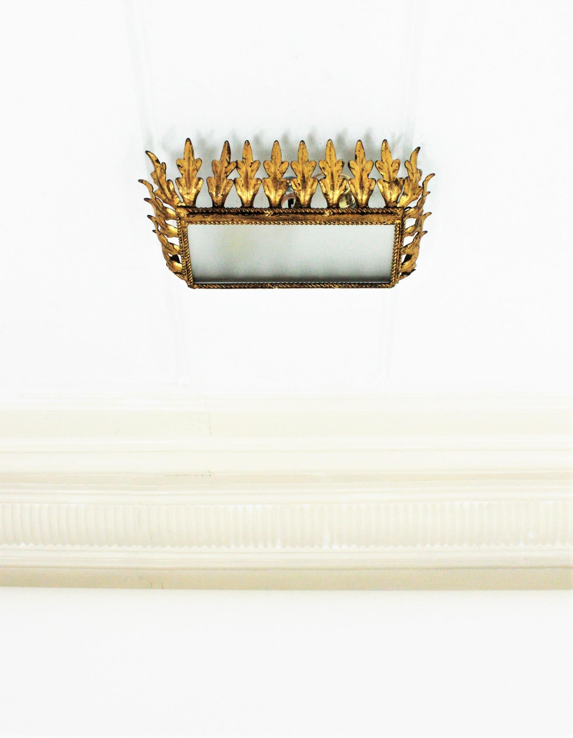 Sunburst rectangular leafed  flush mount with gold leaf gilding and frosted glass shade. Spain, 1950s.
A rectangular gilt iron panel supporting the glass shade is framed by a layer of leaves in sunburst crown disposition.
This eye-catching ceiling