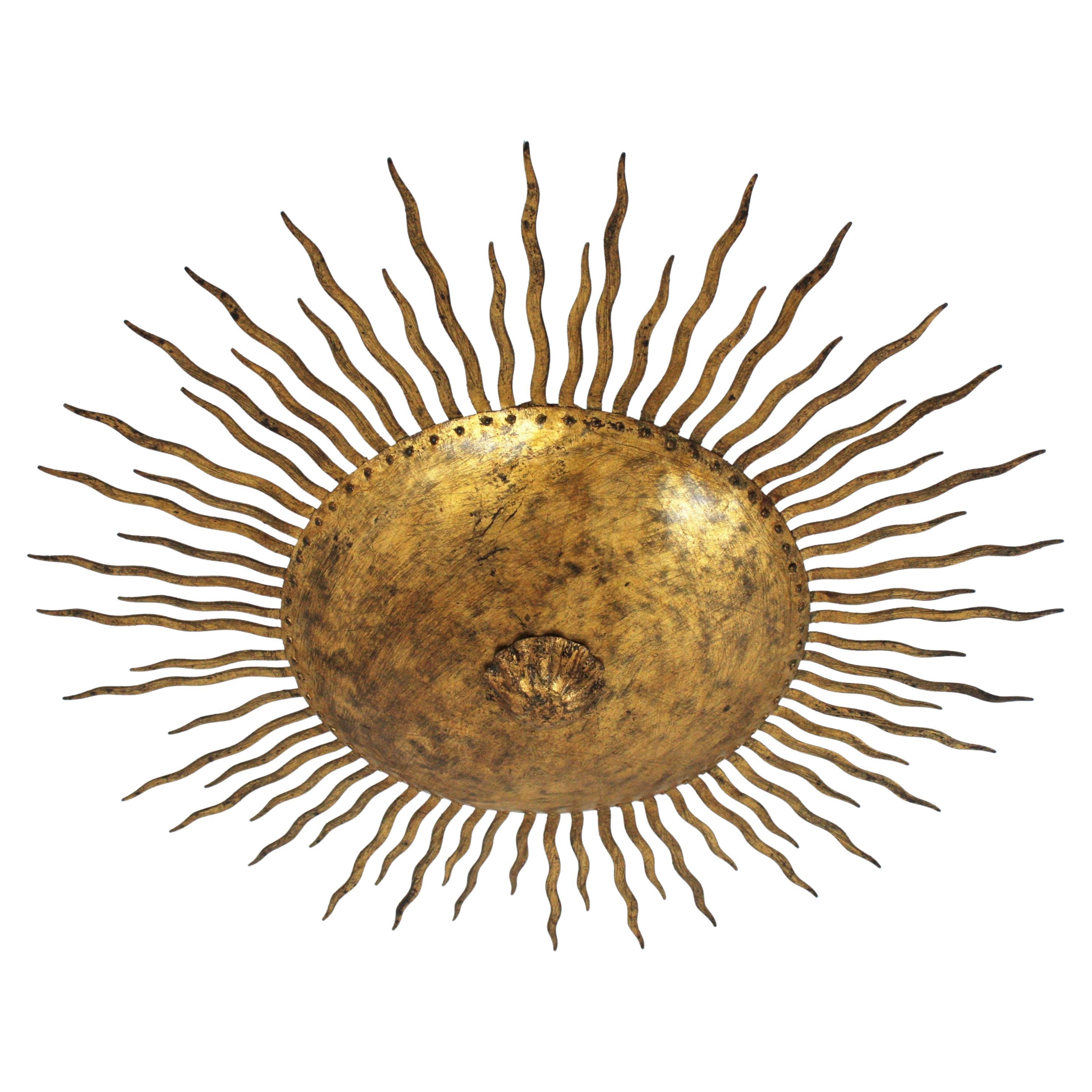 French large wrought gilt hand forged iron sunburst flush mount / ceiling light fixture. France, 1950s.
This hand-hammered iron flushmount has alternating rays in two sizes surrounding the central sphere and a flower decoration at the central part.