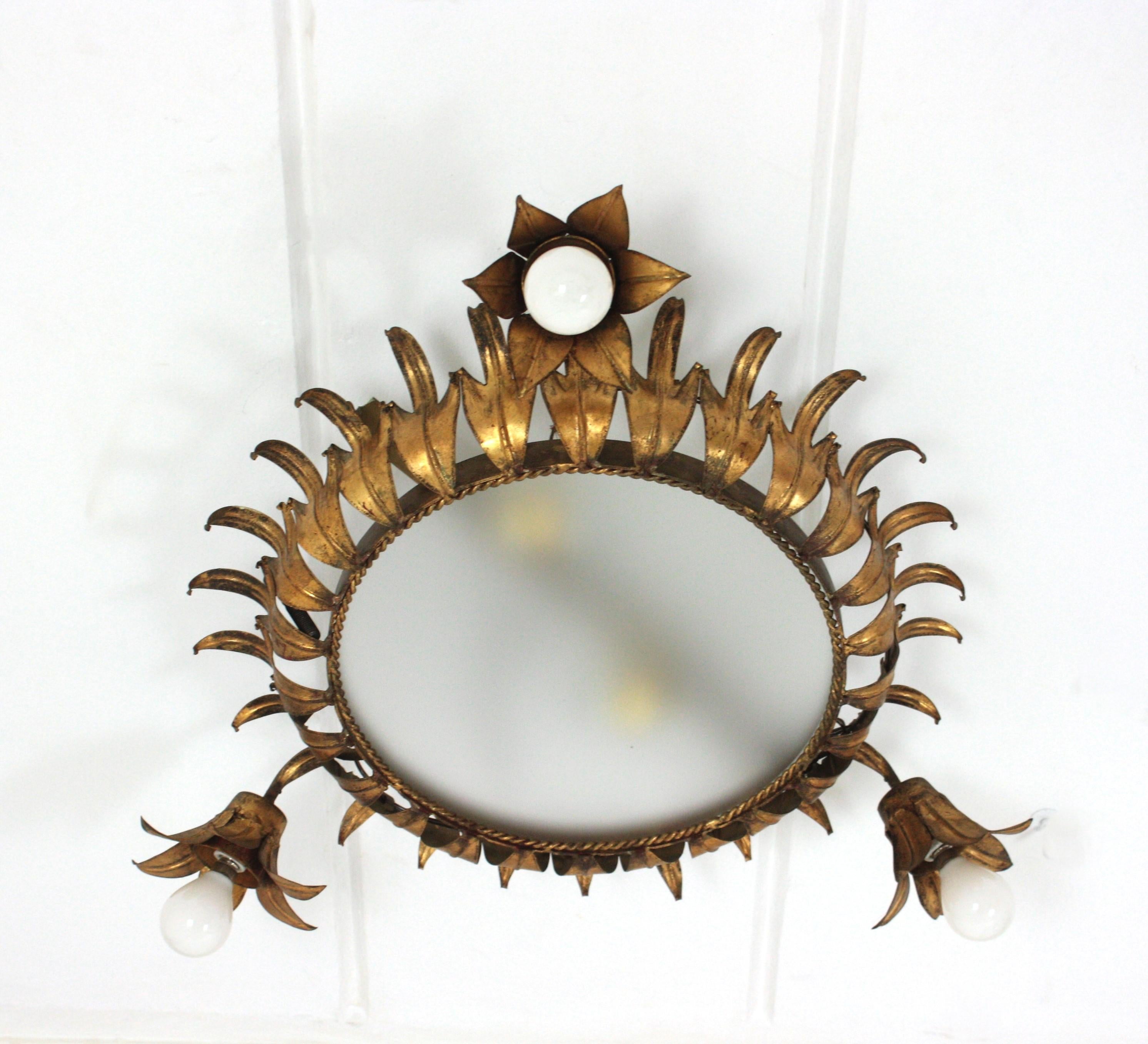 Sunburst Crown Flush Mount with triple flower detail, Gilt Iron. Spain, 1950s
This handcrafted crown sunburst ceiling light fixture features a crown shaped flush mount with frosted glass difusser. The sunburst crown light body is made of iron leaves